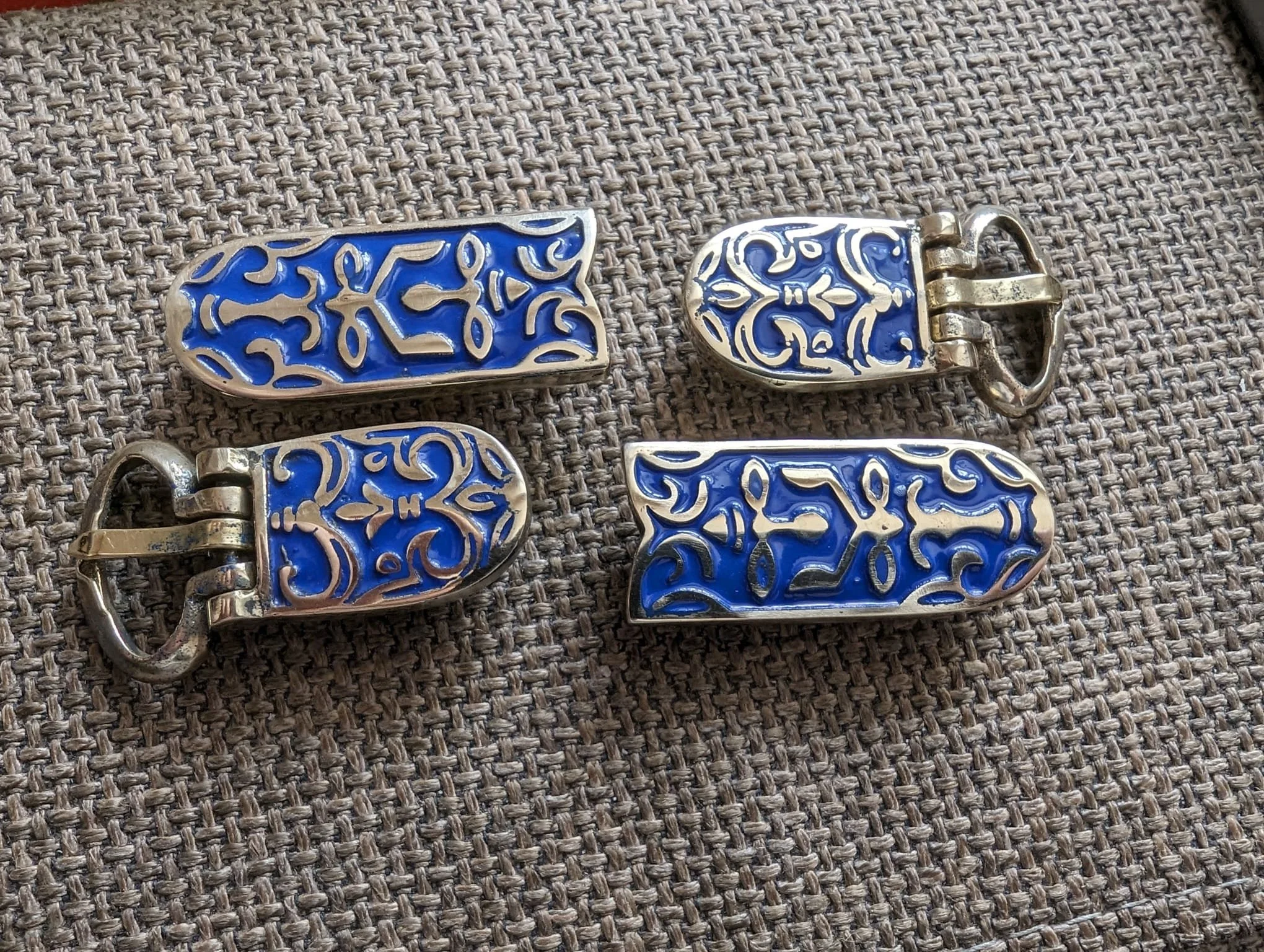 Vier silberne und blaue Schmuckstücke mit filigranen Mustern, zwei davon mit Verschlüssen, auf einem Stoffuntergrund.