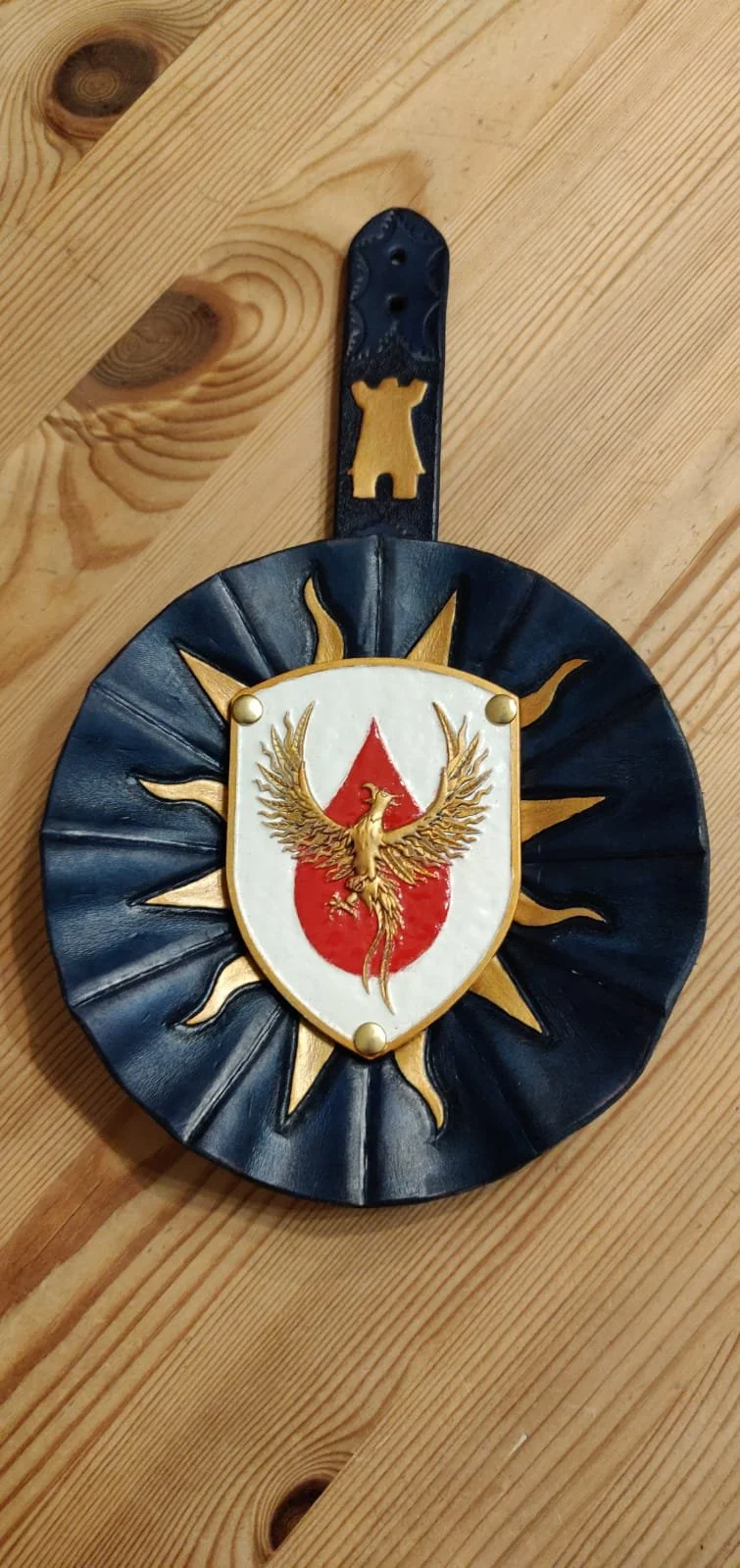 Wandhalter mit Wappen und Sonnenumriss auf Holztisch.