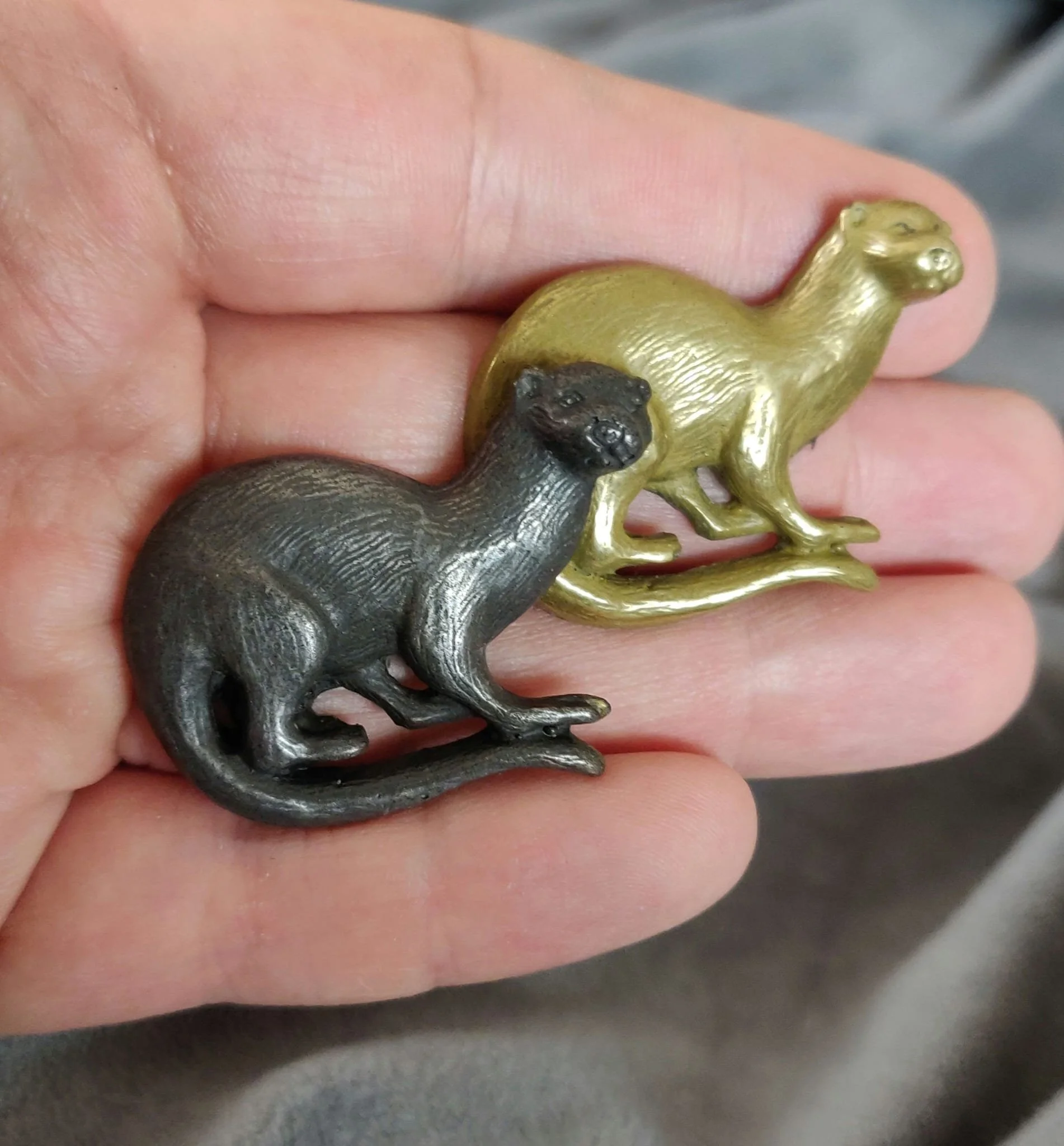Zwei kleine Tierfiguren, eine schwarz und eine goldfarben, die auf einer Hand gehalten werden.