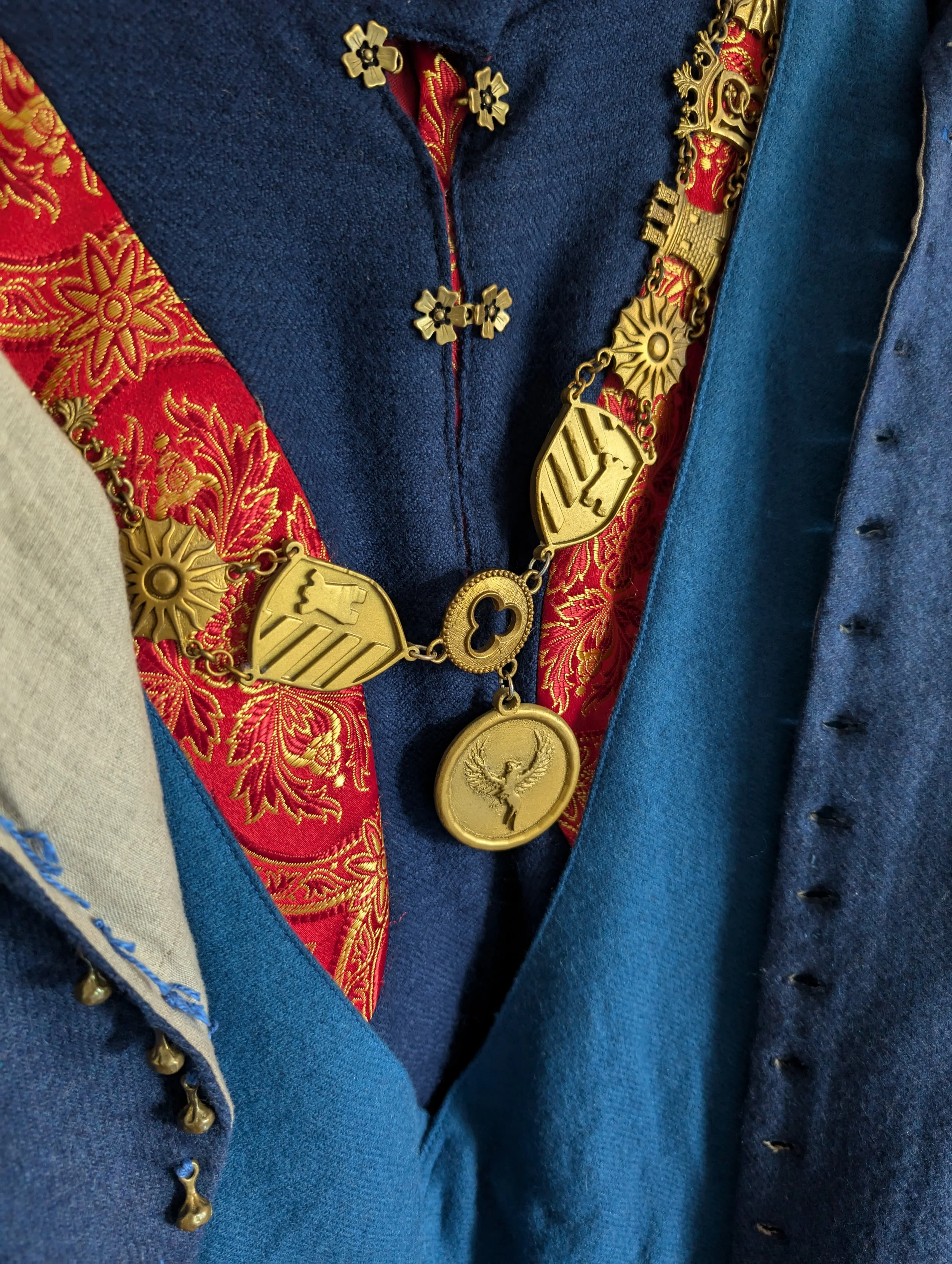 Traditionelle deutsche Kleidung mit einer goldenen Kette über einem blauen Jackett und rotem Inneren mit goldenen Mustern.