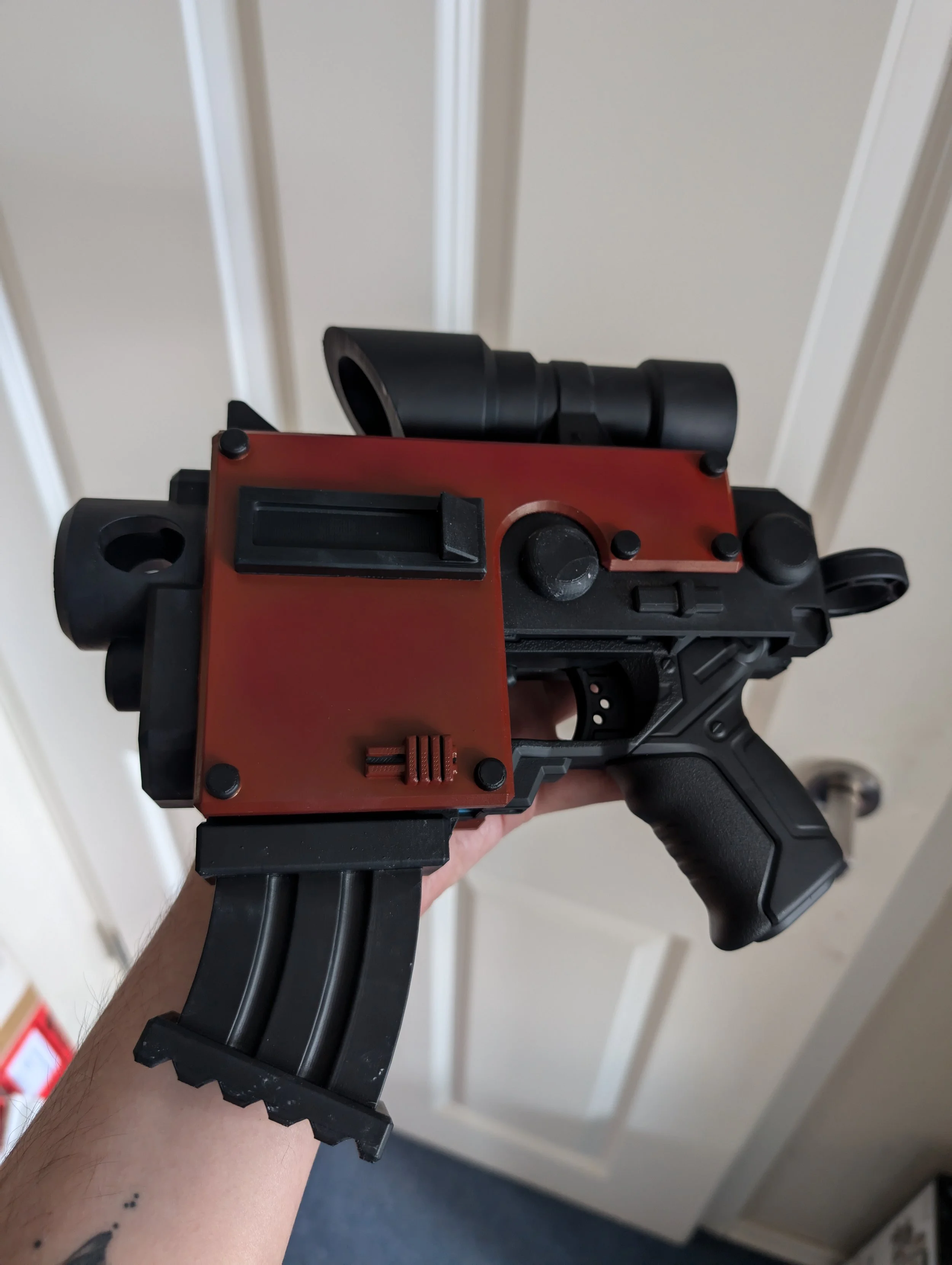 Nahaufnahme eines Spielzeug-Propheten, das einem futuristischen Handfeuerwaffe ähnelt, mit rotem und schwarzem Design und Zielfernrohr.