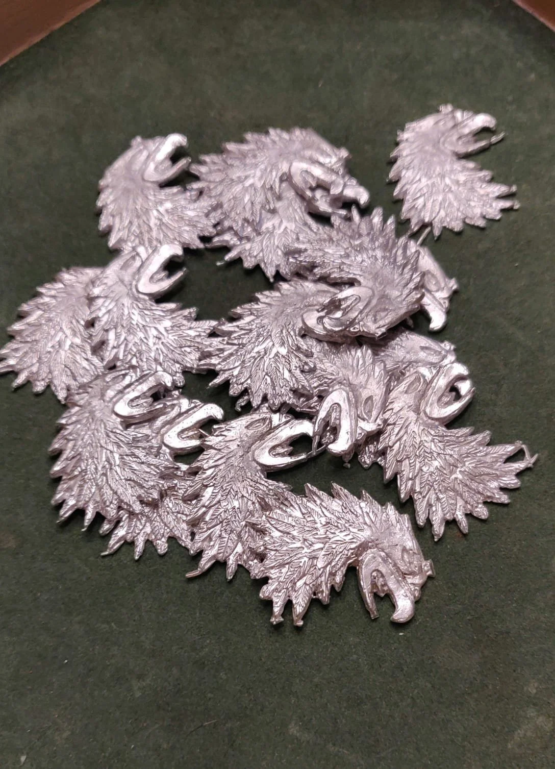 Mehrere metallene Anhänger in Form von Adlerkopffedern auf einer dunklen Oberfläche.