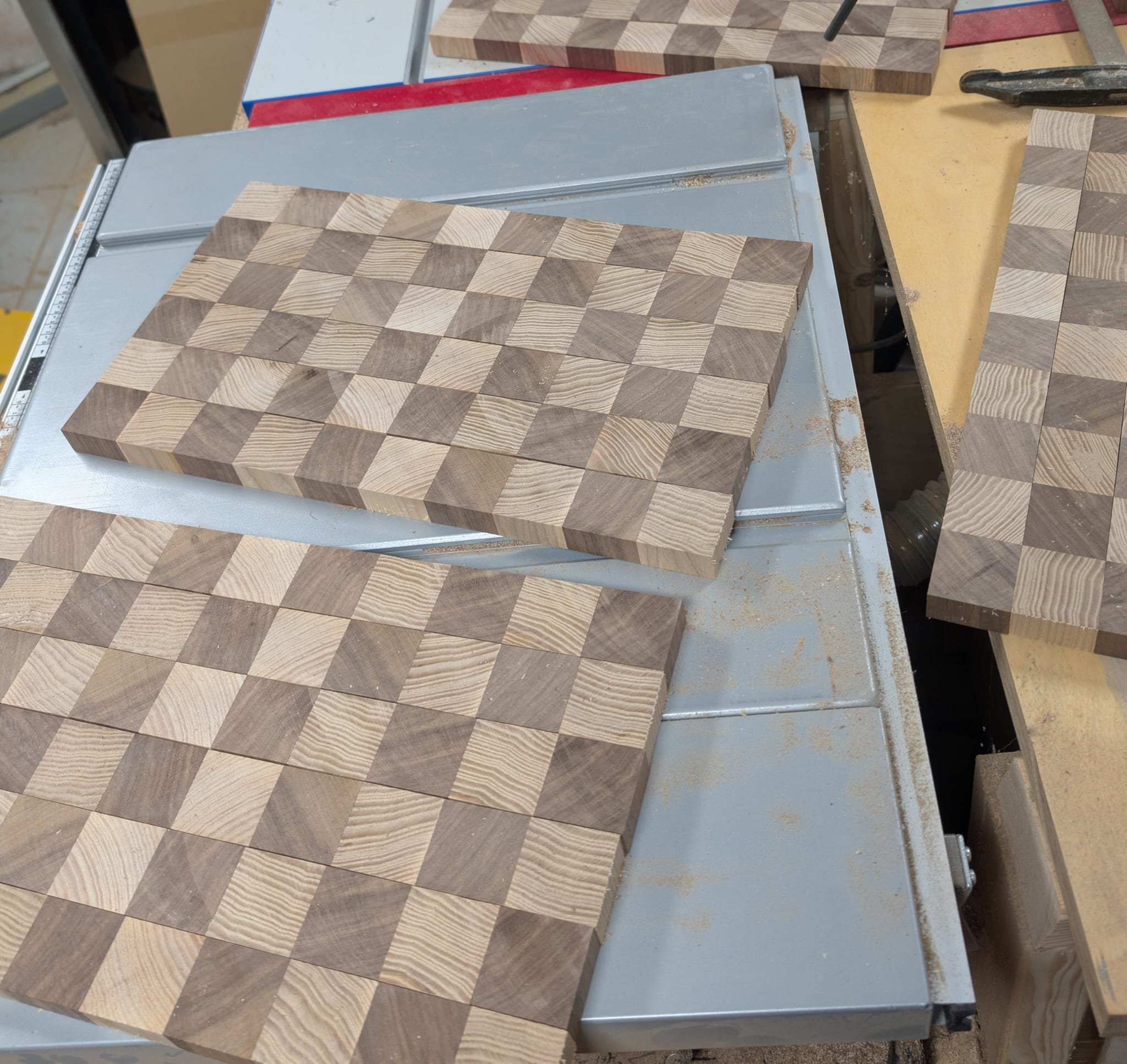 Mehrere gefertigte Schachbretter aus Holz auf Werkbank in einer Werkstatt.