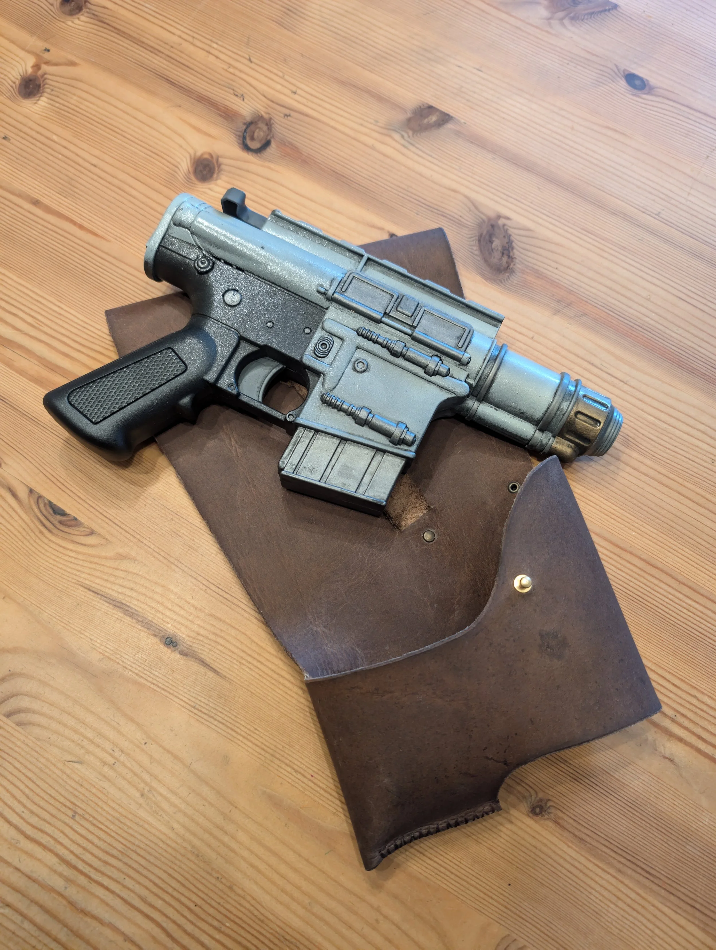 Nachbildung einer futuristischen Pistole auf einem braunen Lederetui, auf einem Holztisch.