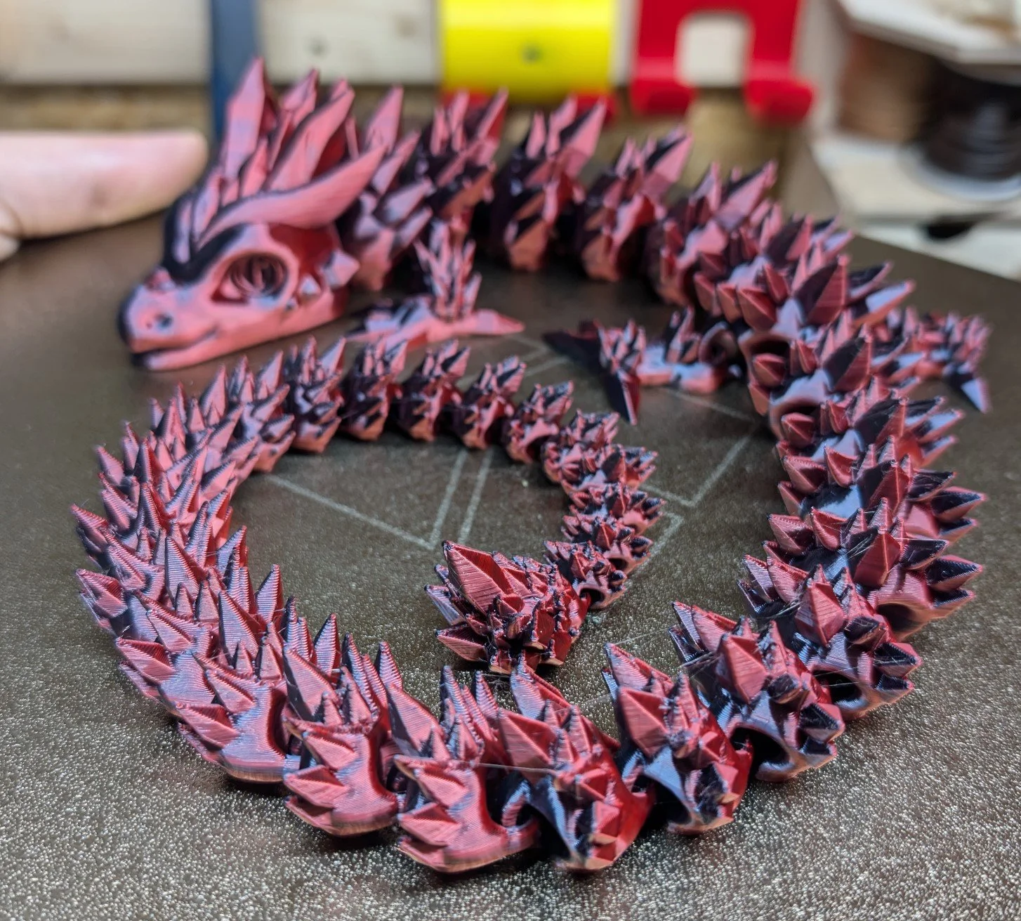 Eine 3D-gedruckte Drachenfigur mit roten und schwarzen Farben, die auf einem schwarzen Tisch liegt.