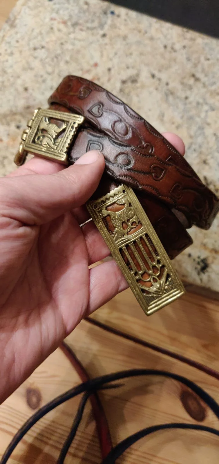 Hand hält einen braunen Ledergürtel mit goldfarbenen Schnallen.