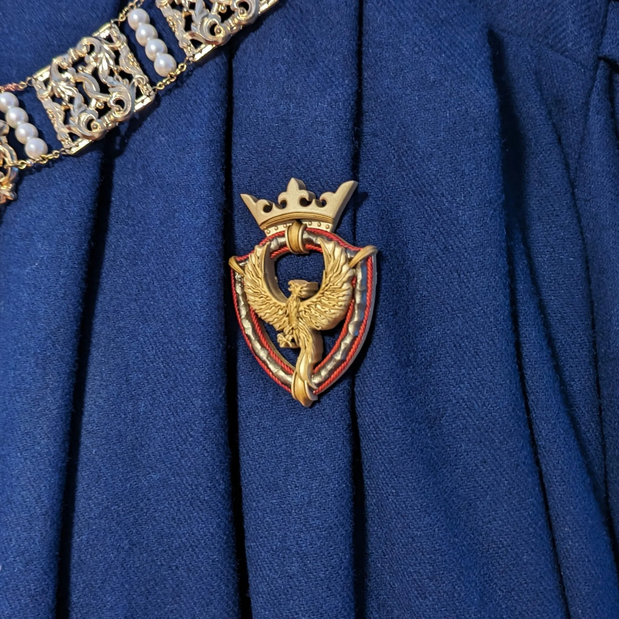 Eine goldene Abzeichen mit einem Adler, einem goldenen Krone oben und roten, weißen und schwarzen Umrandungen, befestigt an einer blauen, gerippten Uniform.