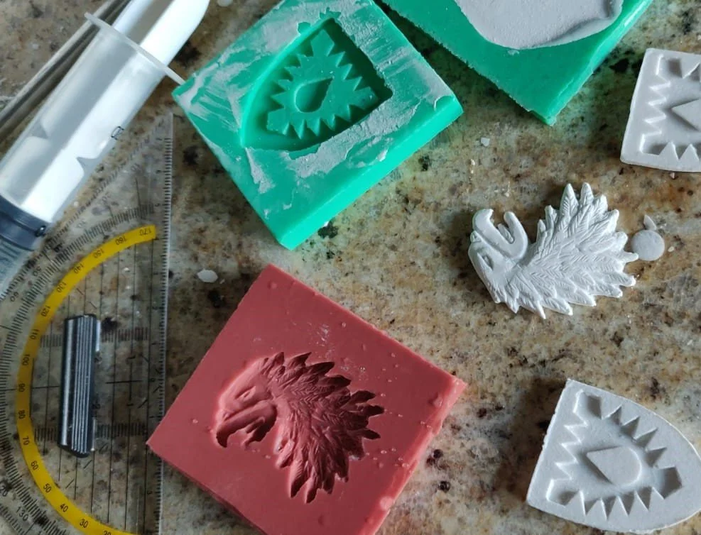 Bunte Seifenstücke mit Einhorn- und Gesichtsrelief, Schneidematte, Lineal und Schneidewerkzeug auf einer Arbeitsplatte.