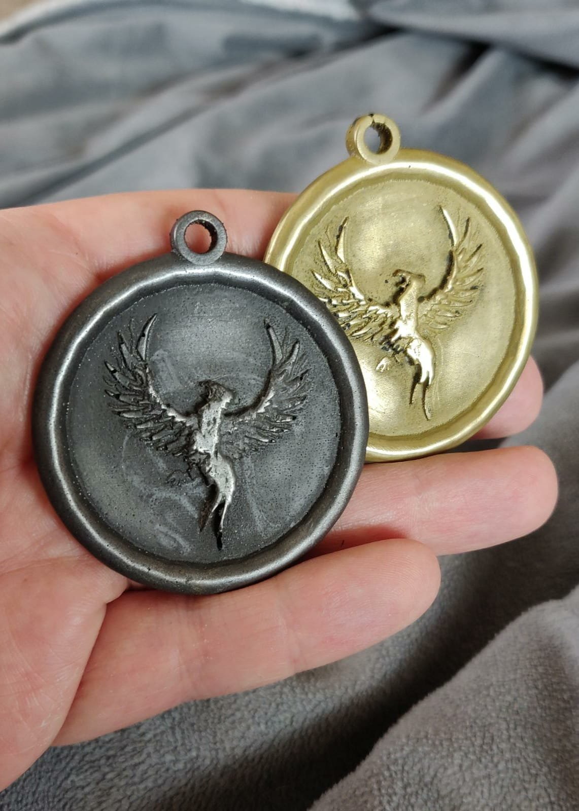 Zwei Medaillen mit einem phoenix-Design, eine goldene und eine silberne, vor einem grauen Hintergrund.