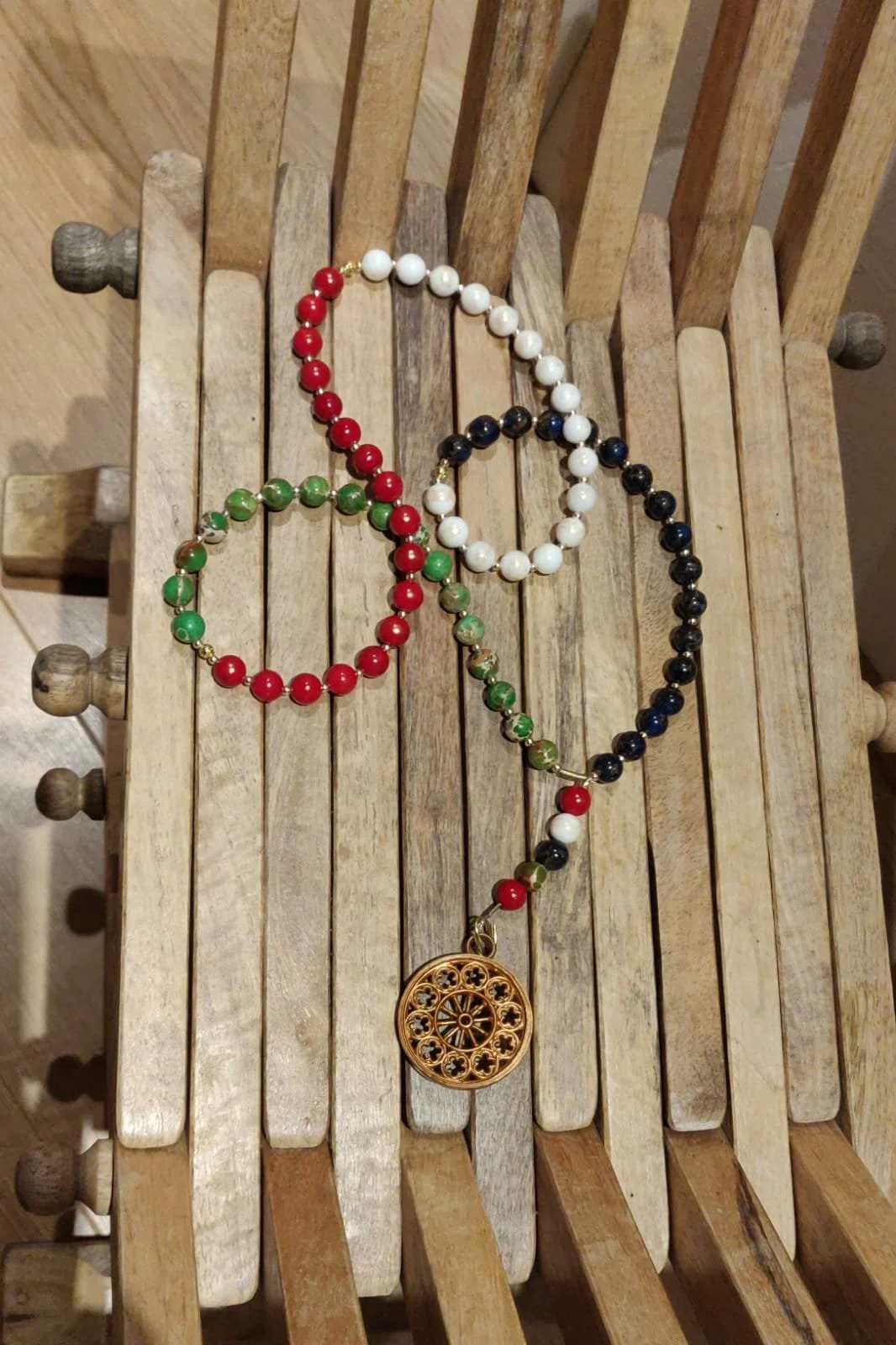 Fünf bunte Perlenketten mit einem goldfarbenen Anhänger auf einem Holzdrehstuhl