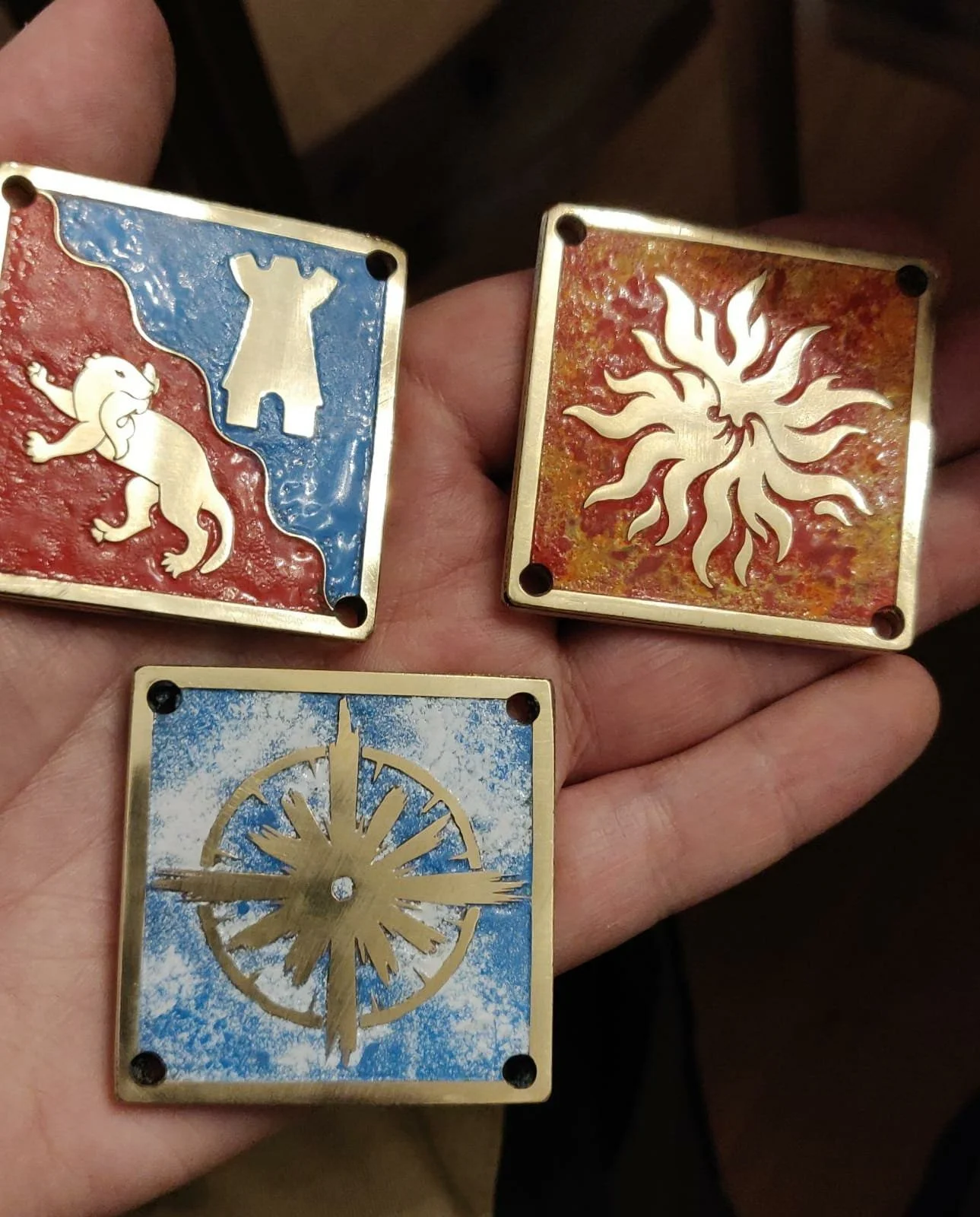 Drei kunstvolle, goldene Würfel mit verschiedenen Wappen und Symbolen, einer mit einer Sonne, einer mit einem Löwen und einer mit einem Rad.