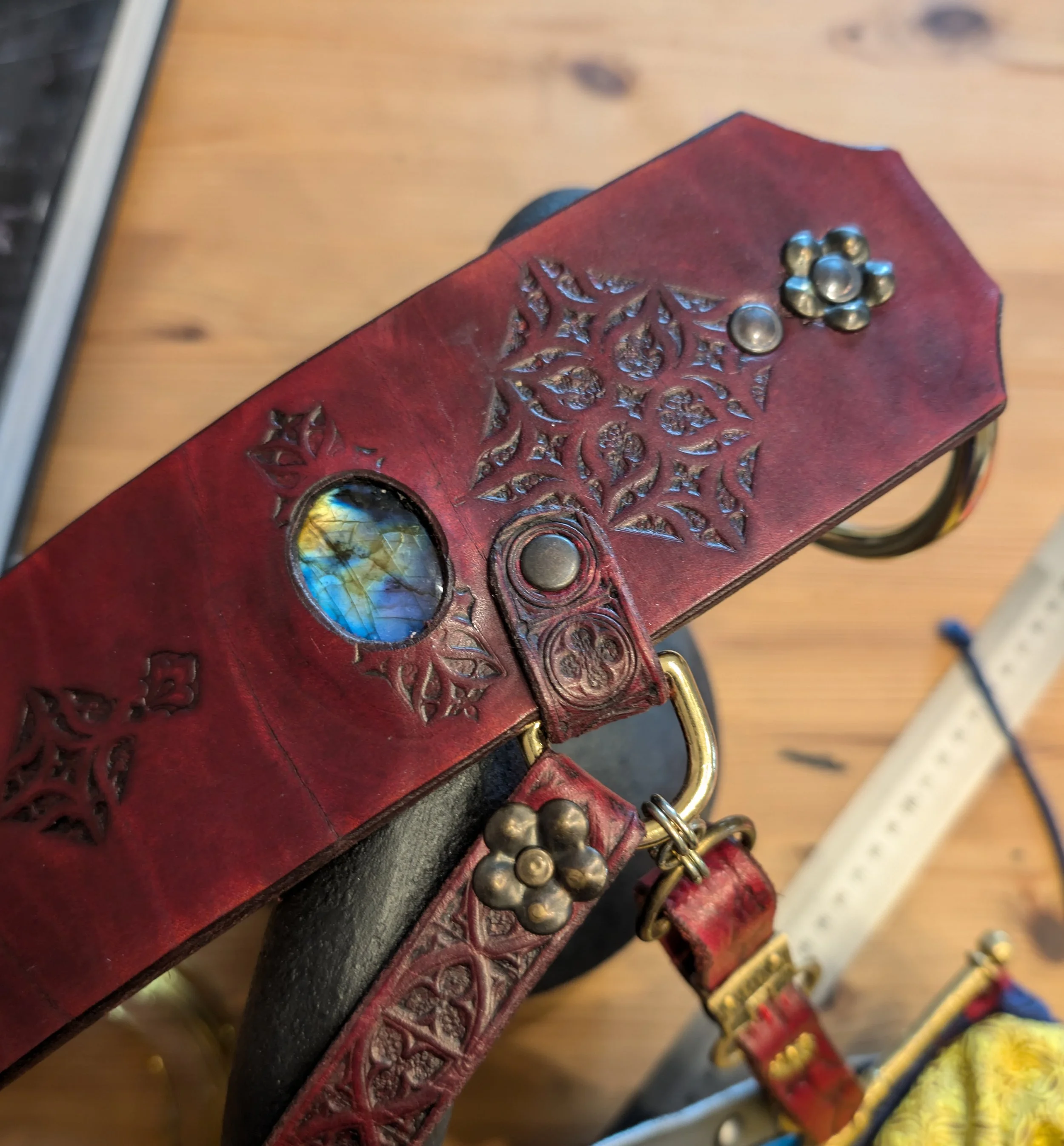 Ein rote Lederschutz für ein Tierhalsband mit einem lilafarbenen und blauen Glasstein und metallenen Verzierungen.