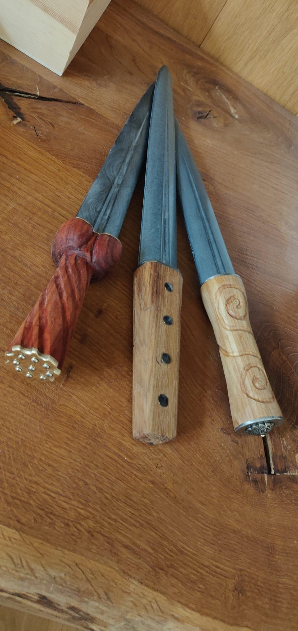 Drei Messer mit unterschiedlichen Holzgriffen liegen auf einem Holztisch.