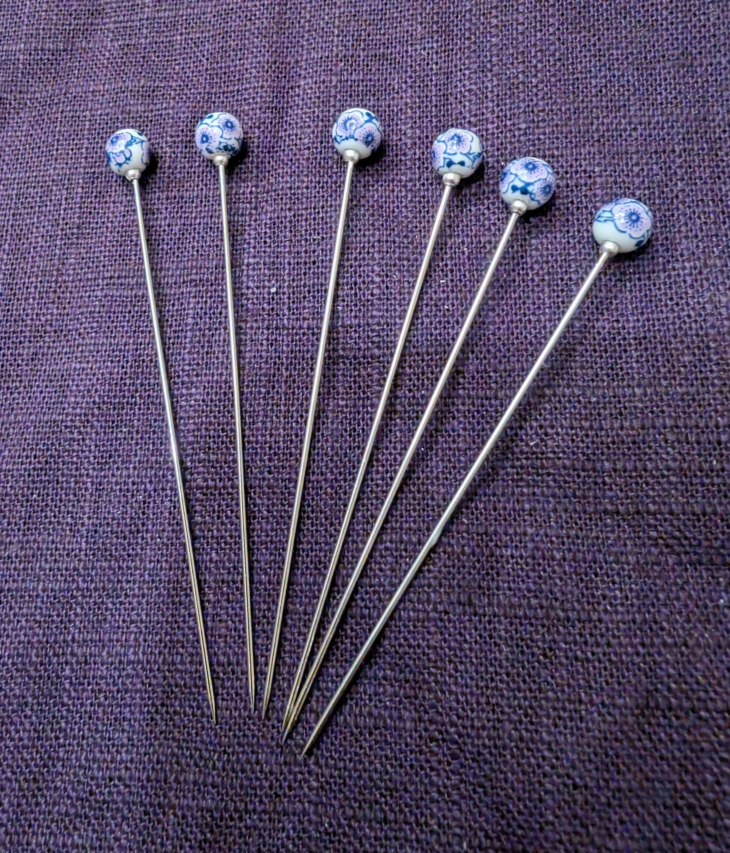 Sechs Zackennadeln mit blauer und weißer Musterung auf lila Stoff