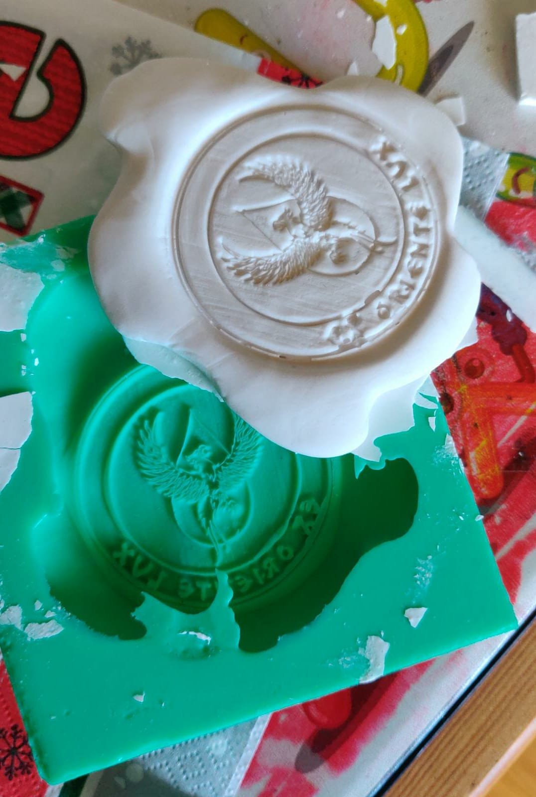 Seife mit einem eingravierten Logo eines fliegenden Engels, die auf einer grünen Unterlage liegt, mit einem Spiegel, der das Logo reflektiert.