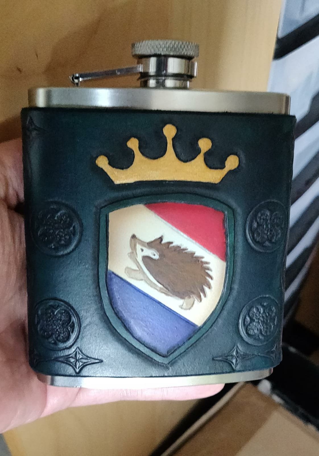 Ein älteres Tabakfläschchen mit Wappen, das einen Hirschkopf zeigt, umgeben von einem schwarzen Lederhüllen mit goldener Krone oben.