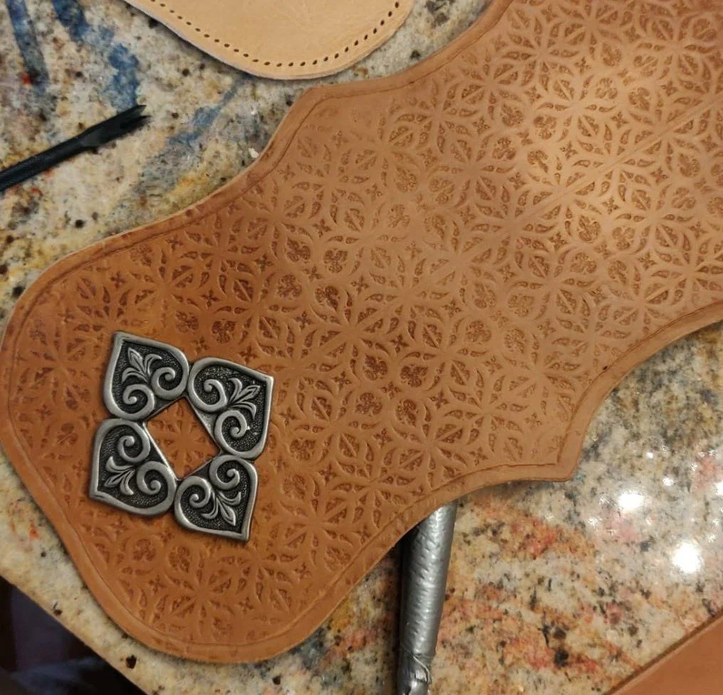 Ein Schnitzmesser auf einer Holzlederarbeit, die ein detailliertes, filigranes Ornament zeigt, vermutlich für die Herstellung von Lederaccessoires.