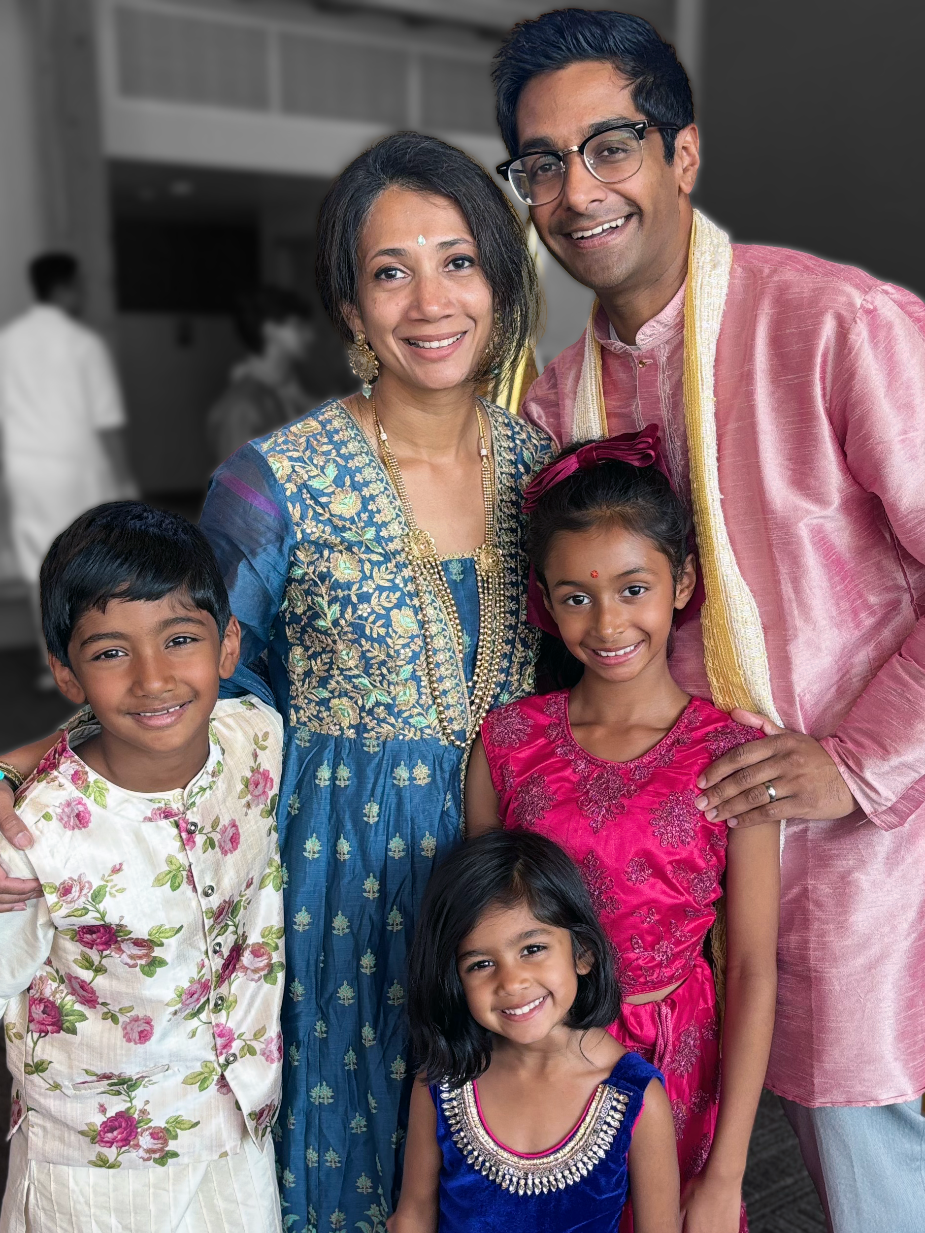 A family of six of Indian descent at a celebration, with the adults dressed in traditional Indian attire and the children in colorful ethnic clothing, smiling at the camera.
