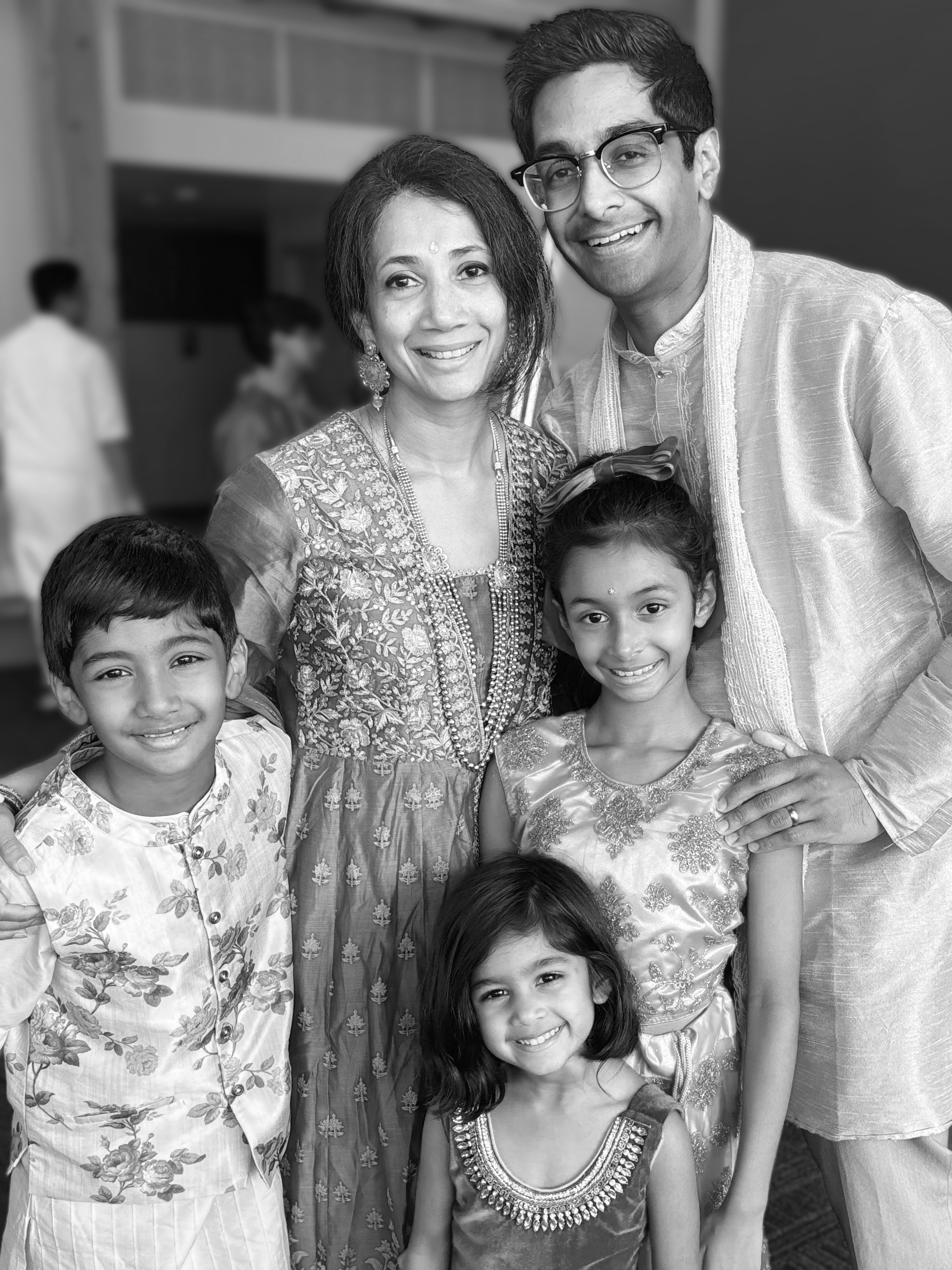 A smiling family of six, including two adults and four children, dressed in traditional Indian clothing, posing together at an indoor event.