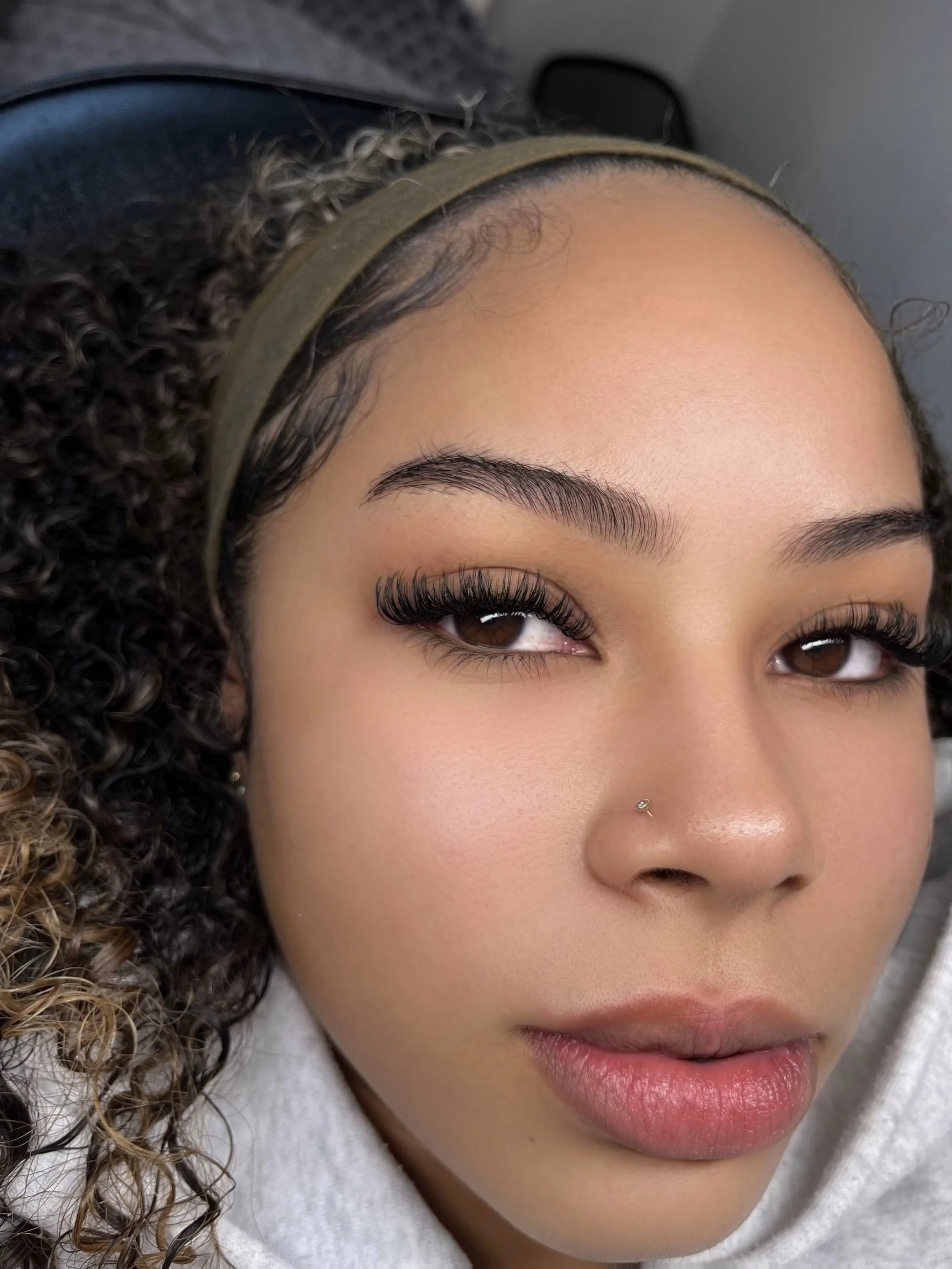 Close-up of a woman with curly hair, wearing a green headband and makeup, lying down with her eyes slightly closed.