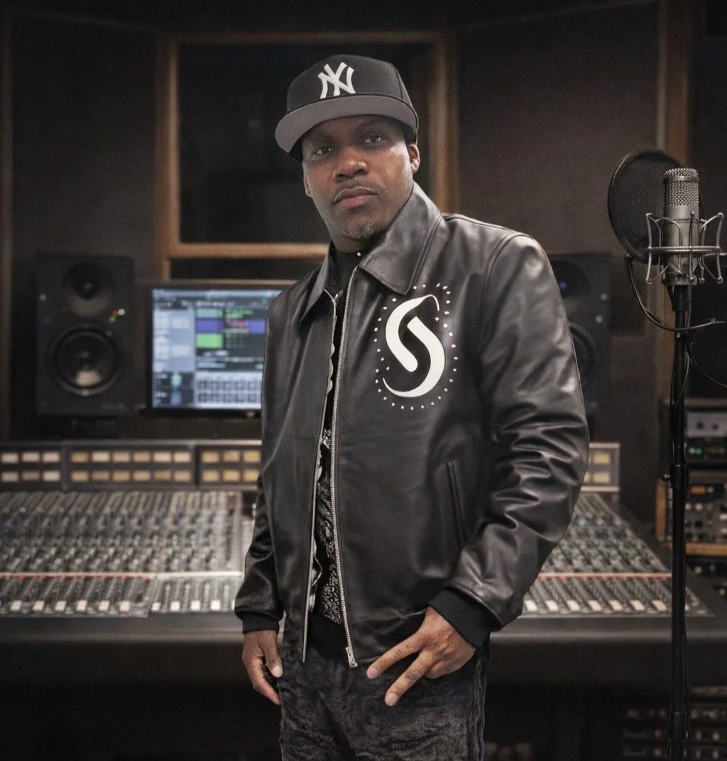 Man in a leather jacket and New York Yankees cap standing in a recording studio.