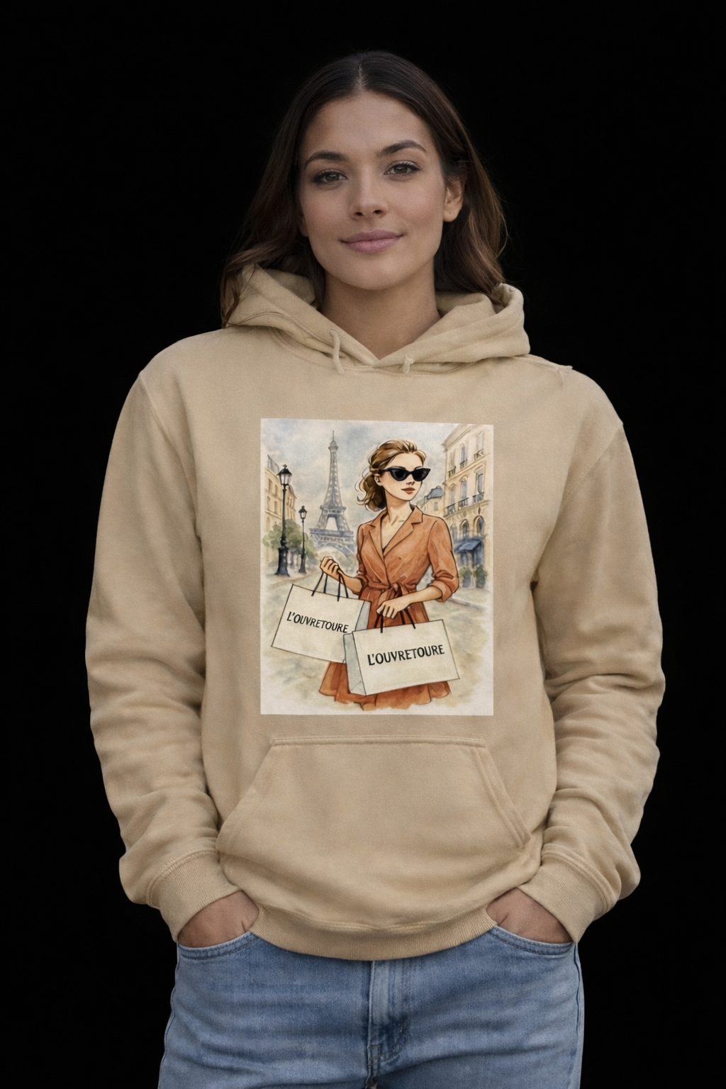 Young woman wearing a beige hoodie with a graphic of a fashionable woman with shopping bags and the Eiffel Tower in the background.