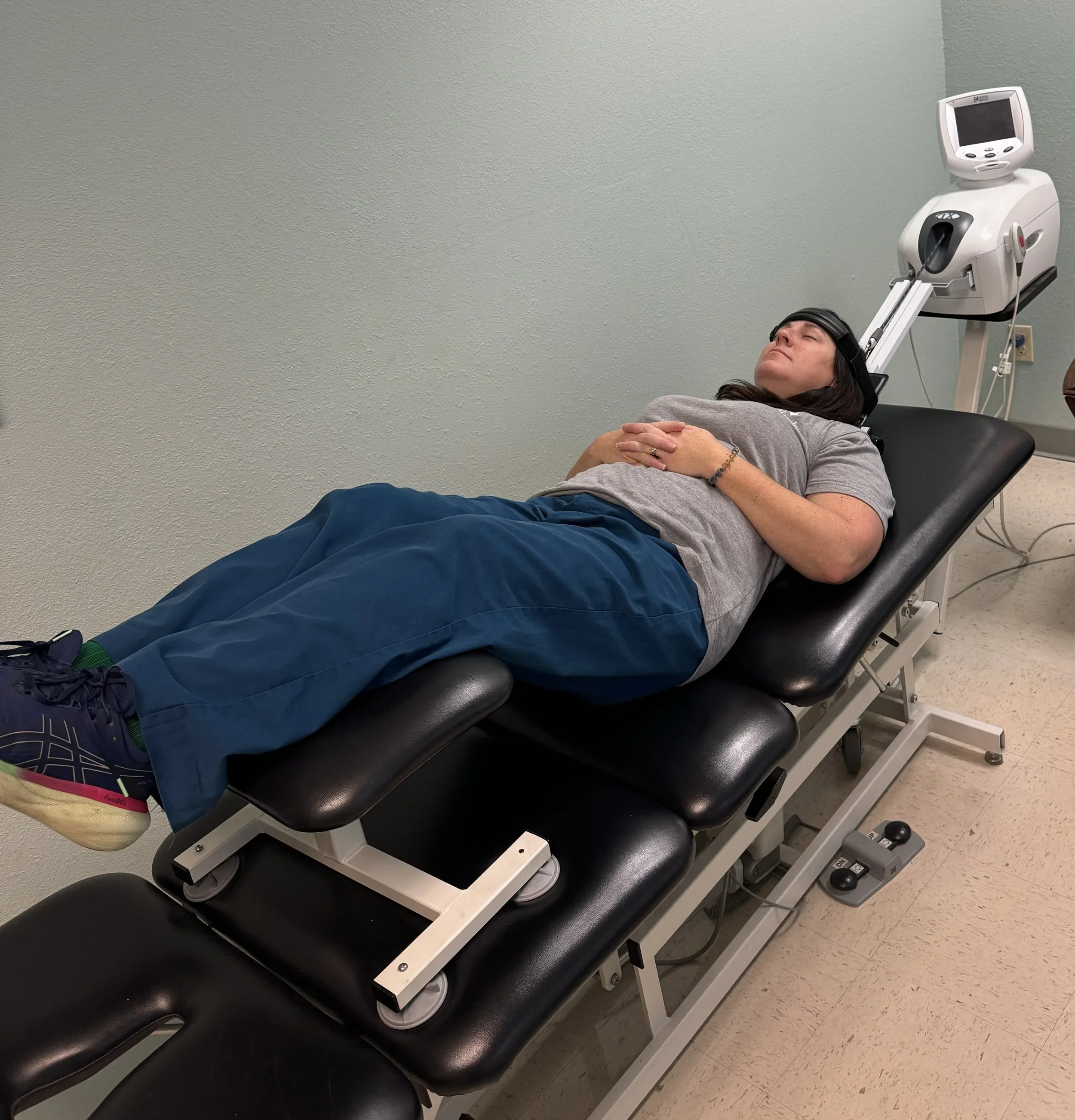 A woman lying on a medical examination table with head in a head coil, in a healthcare setting, possibly undergoing an MRI scan.