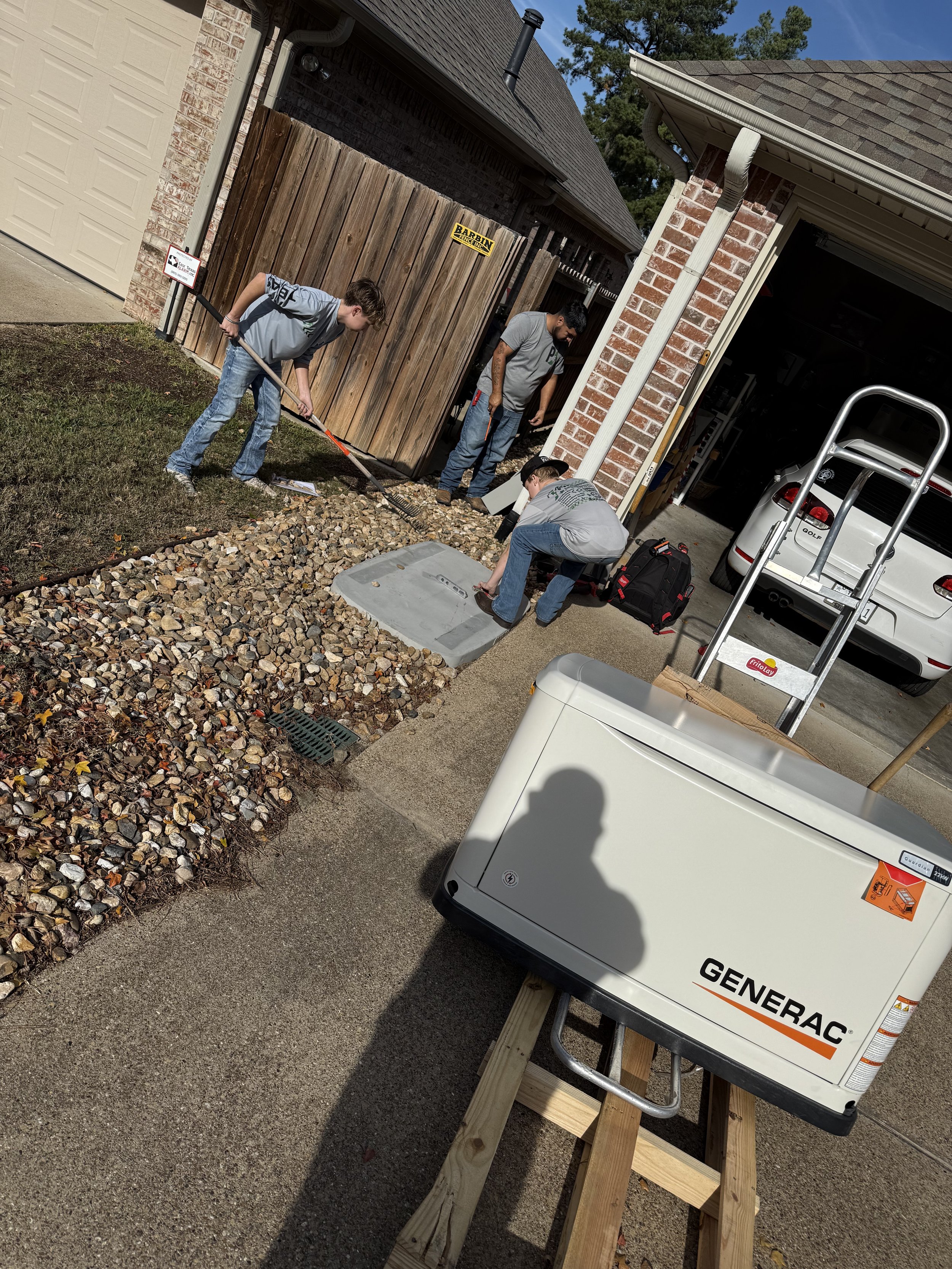Group of young men installing a protective cover over an underground utility access point in a residential backyard, with construction tools and a generator visible.