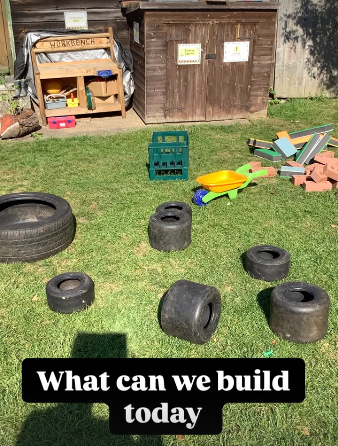 A backyard with tires, bricks, and toy tools scattered on the grass, indicating a space for children's play or outdoor building activities.