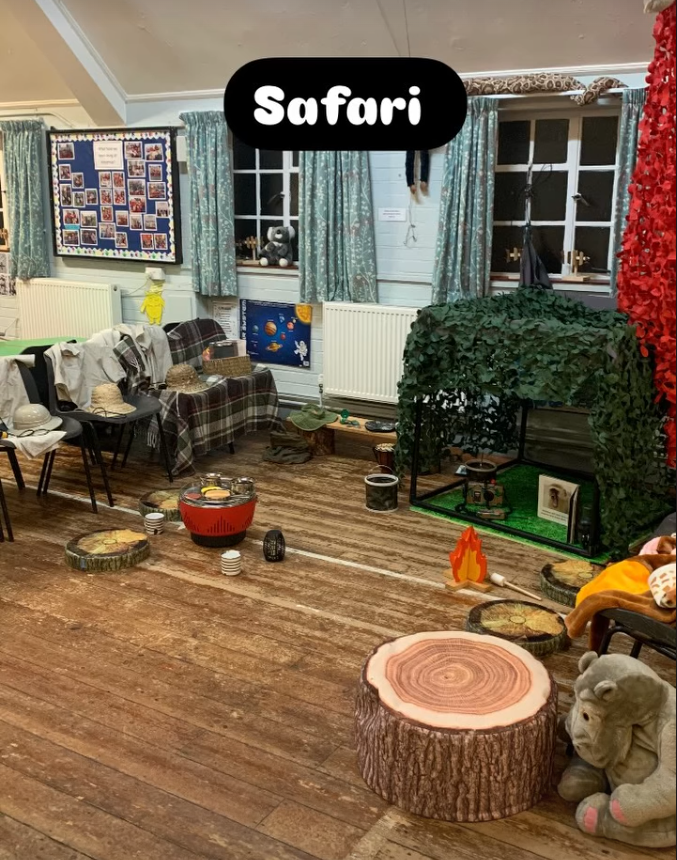 Room decorated for a pretend safari adventure with a faux animal enclosure, logs, a fire prop, and safari-themed decorations.
