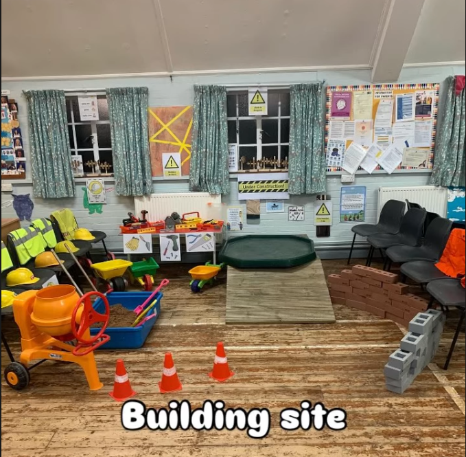 Indoor children's play area with toy construction equipment, cones, safety helmets, pretend tools, and a small ramp, indicating a building site theme for kids.