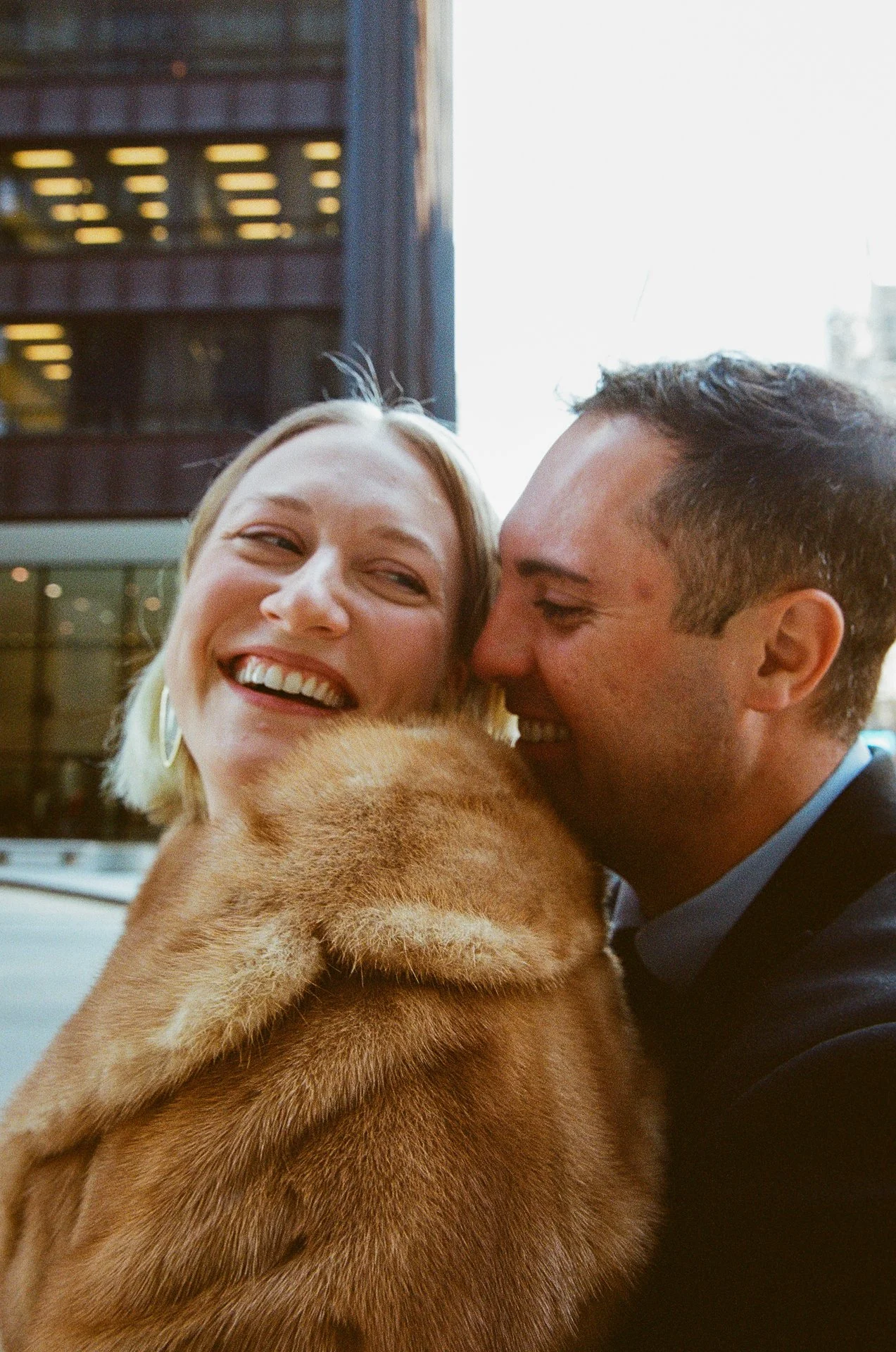 A smiling woman and man are close together, with the woman wearing a fur coat and both enjoying the moment.