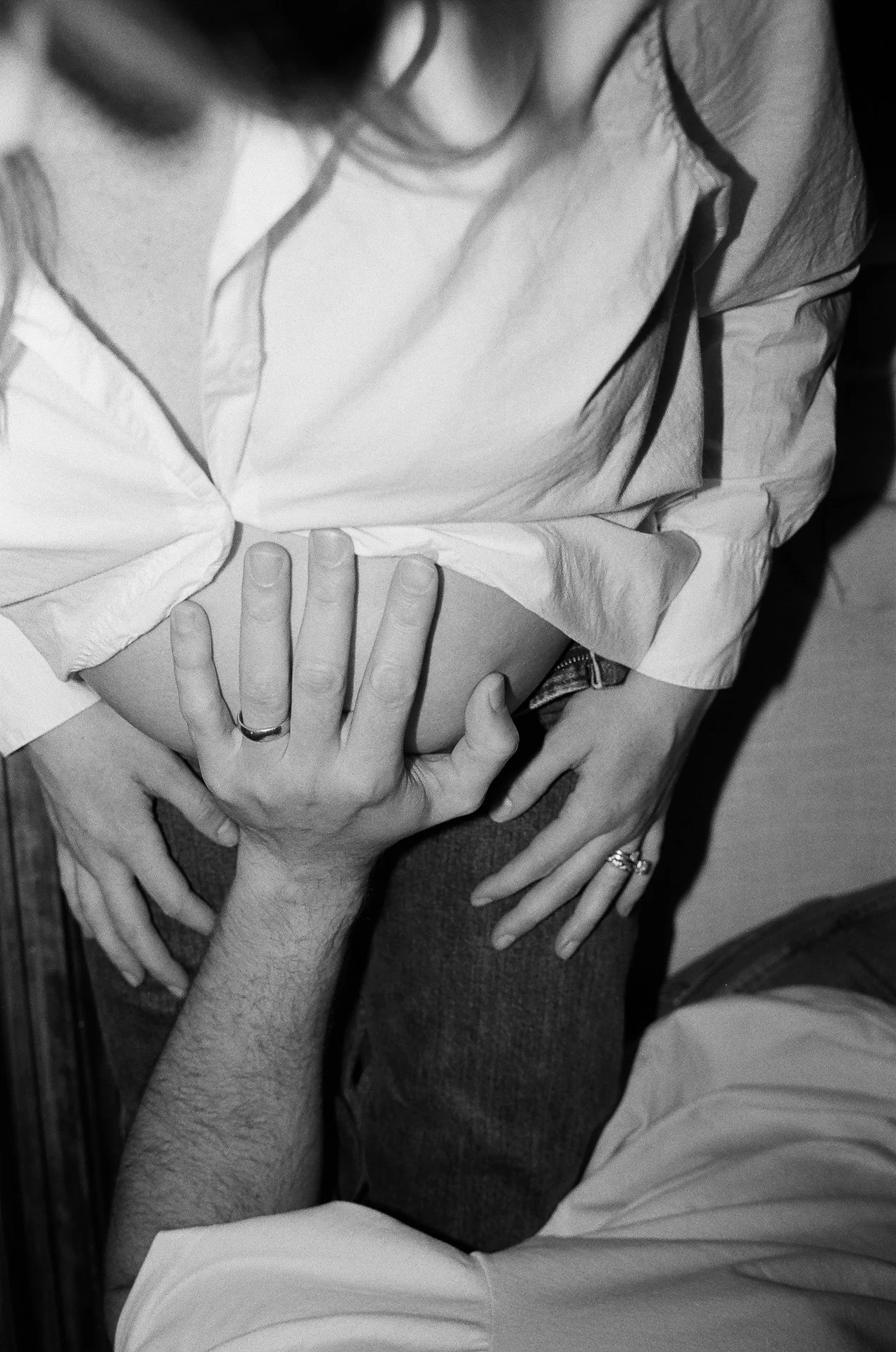 Black and white photo of two people, one sitting and one hand reaching around, with their hands overlapping on the person's waist, and their faces not visible.