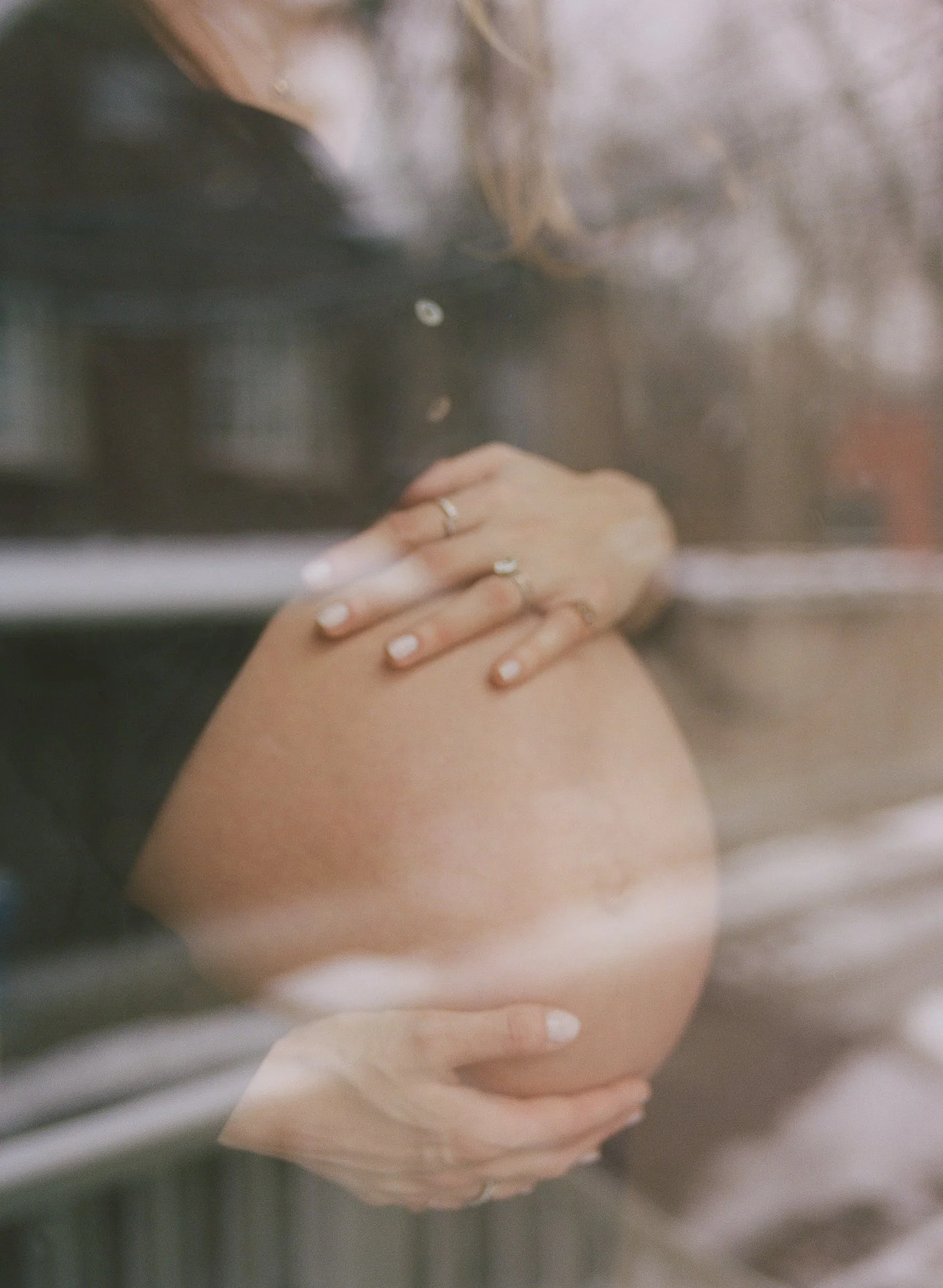 A person with a ring on their finger holding their pregnant belly through a window or glass surface.