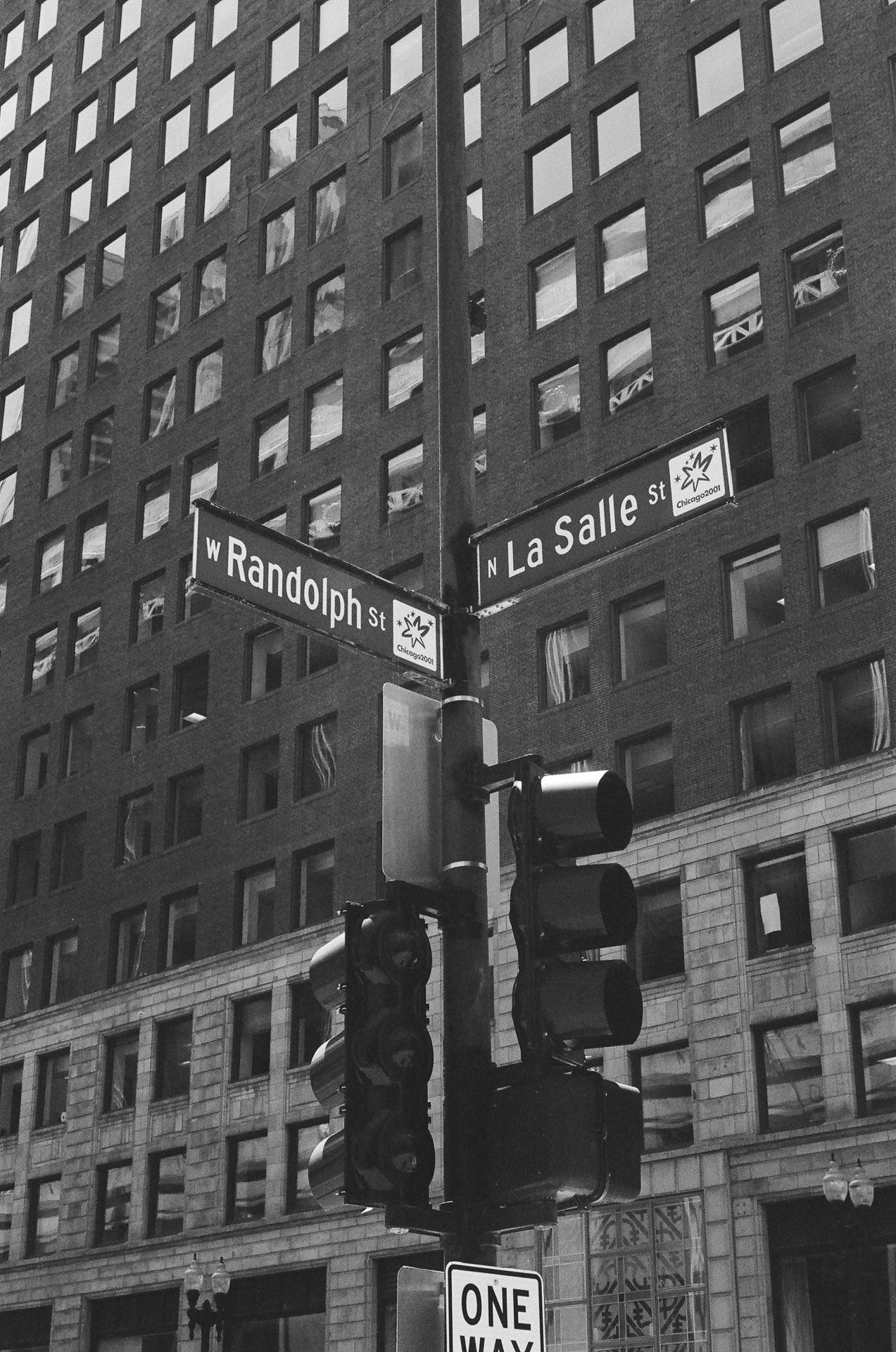 Street signs at the intersection of West Randolph Street and North La Salle Street in Chicago, with a traffic light and a high-rise building in the background in black and white.