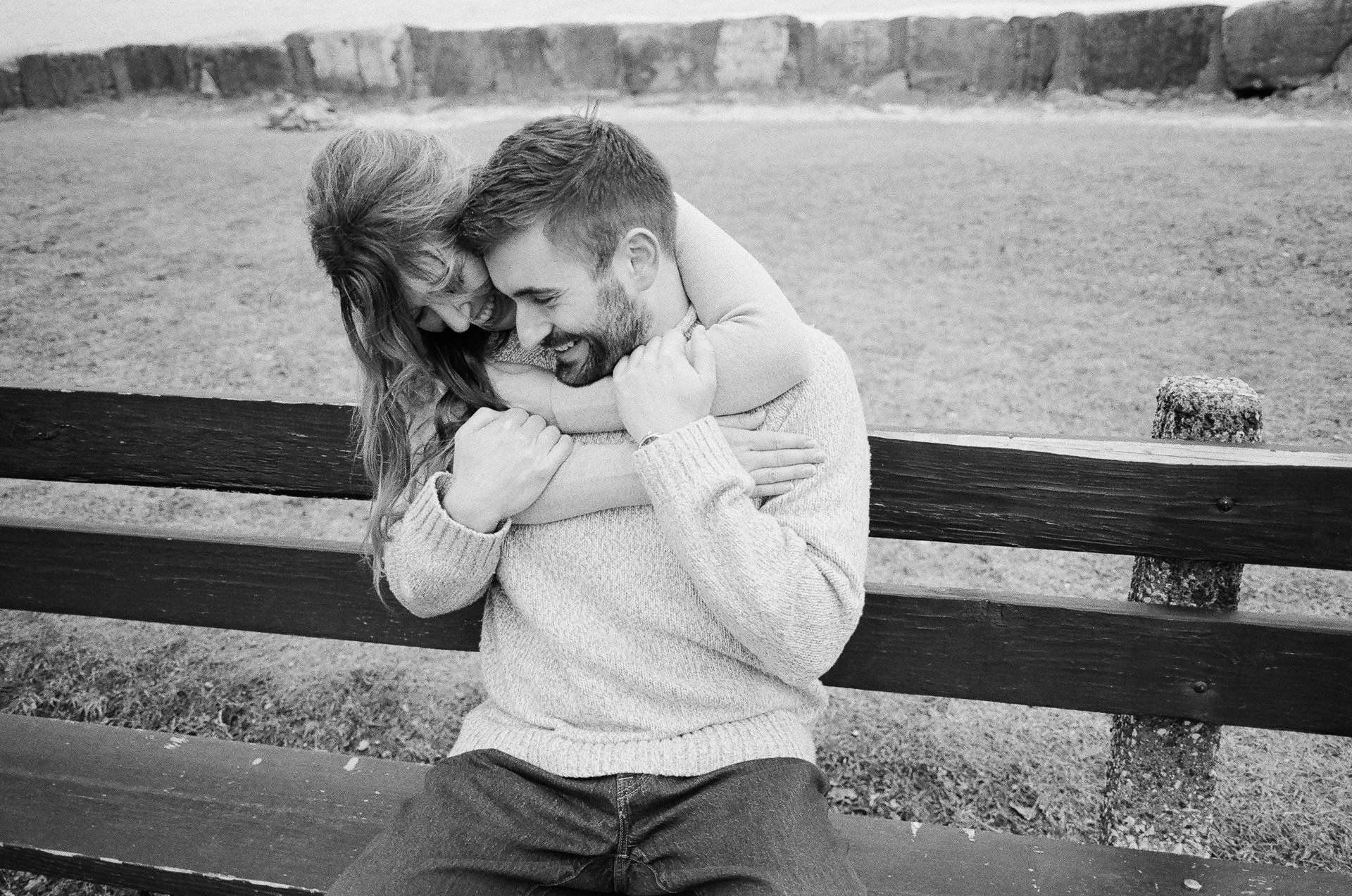 A man and woman sharing a joyful embrace on a park bench, smiling and hugging.