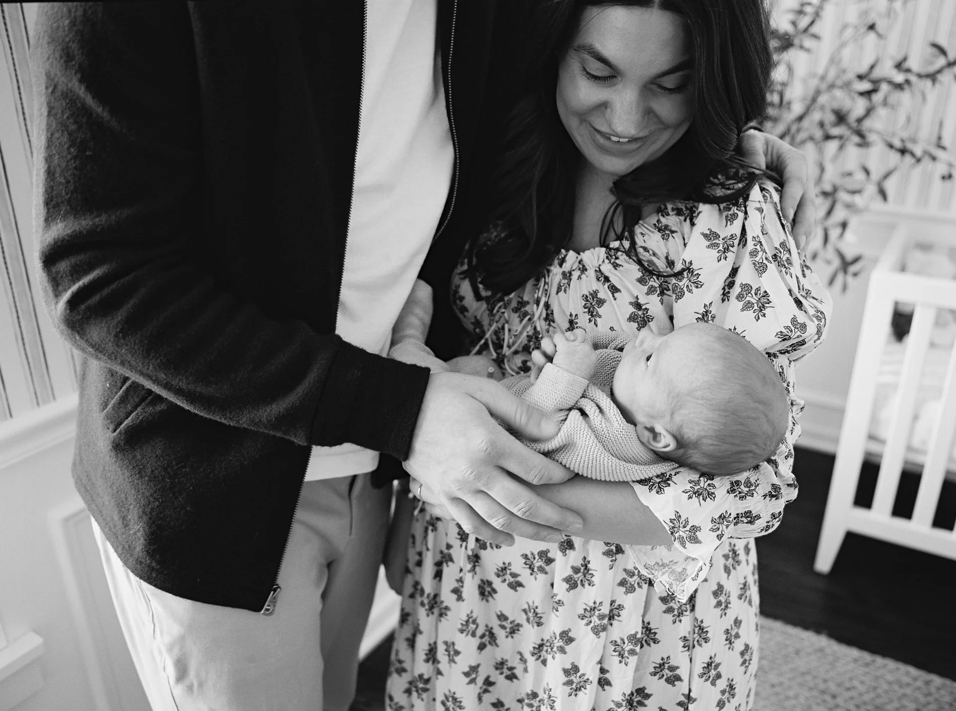 A woman holding a newborn baby while a man leans in to see the baby, all smiling and looking at the baby.