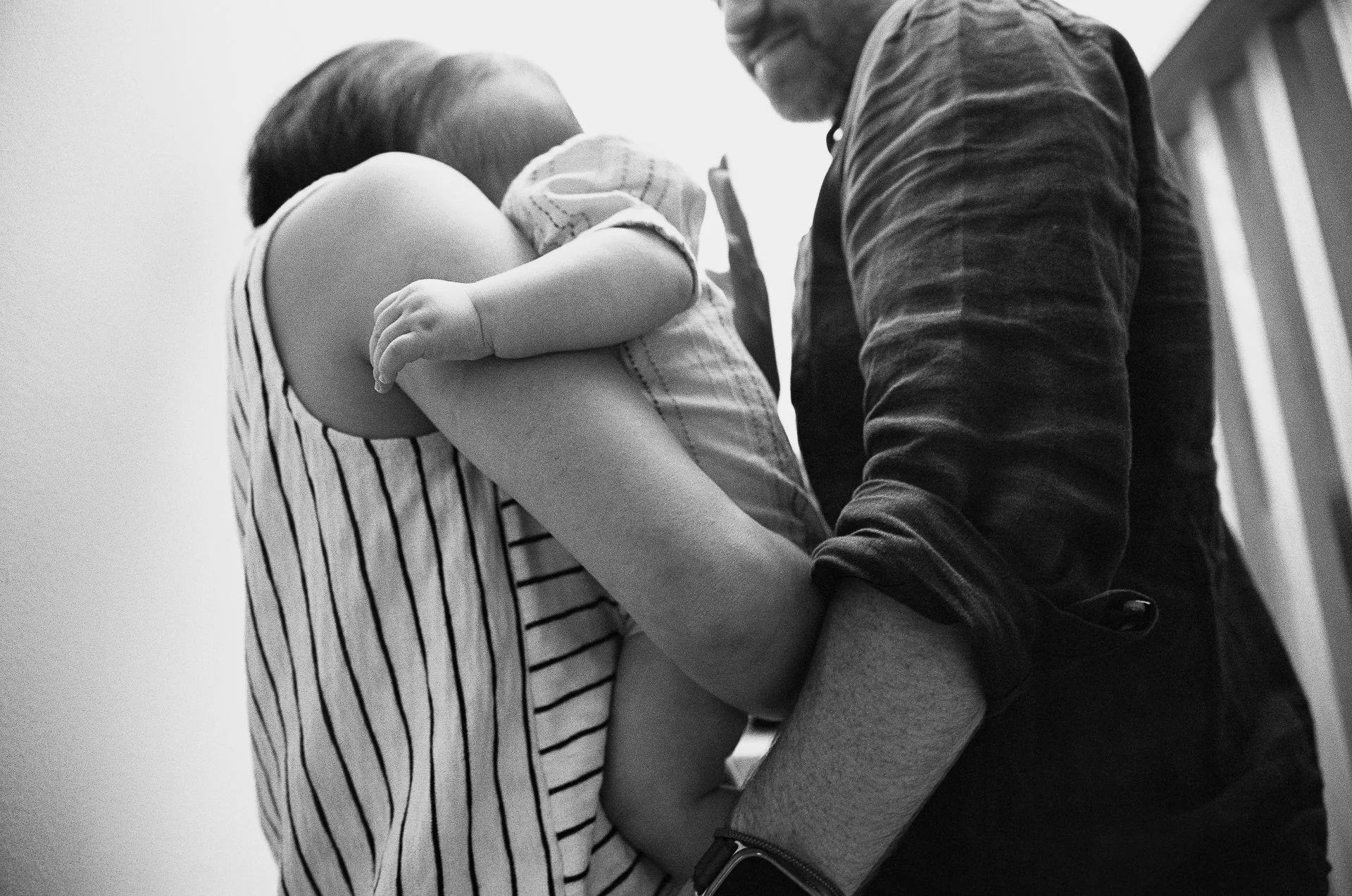 A woman holding a child in her arms, with the child's face turned away and the woman’s face not visible. The image is black and white.