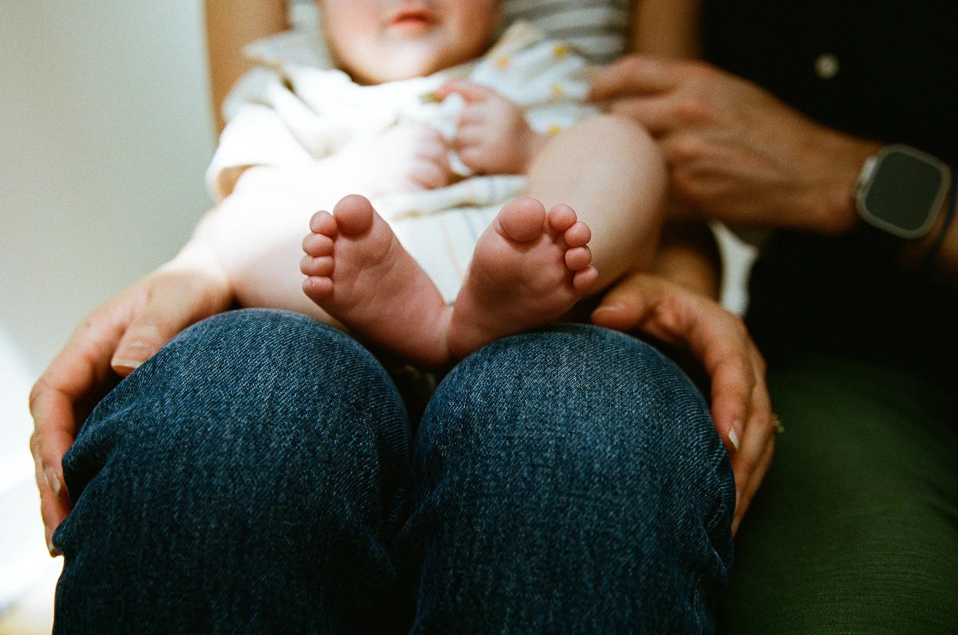 A baby lying on an adult's lap, with close-up of baby's tiny feet and lower legs, wearing a colorful striped outfit.