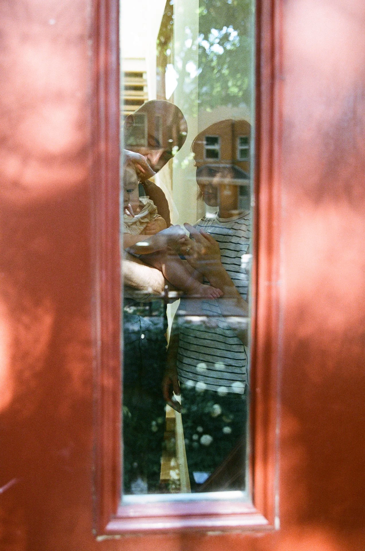 Reflection of a woman, a child, and a person using a smartphone, seen through a glass door with a wooden frame.