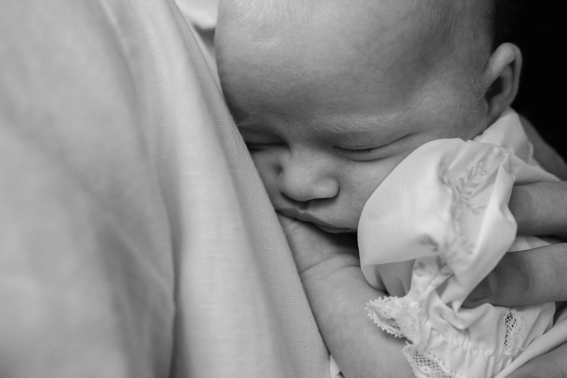 A young child peacefully sleeping on an adult's chest, gently hugging their finger, in black and white.