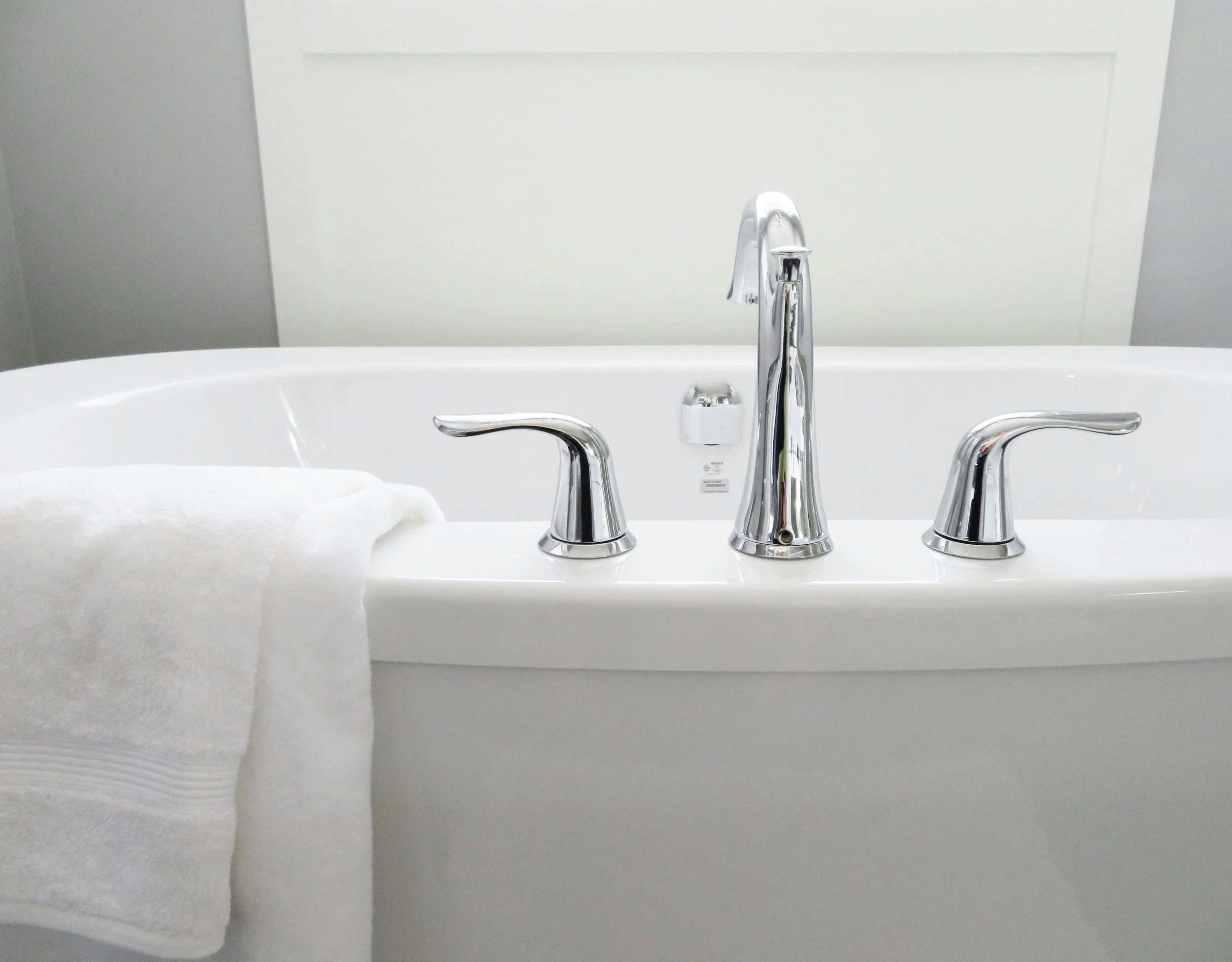 Close-up of a white bathtub with a shiny silver faucet and handles, and a white towel draped over the side.
