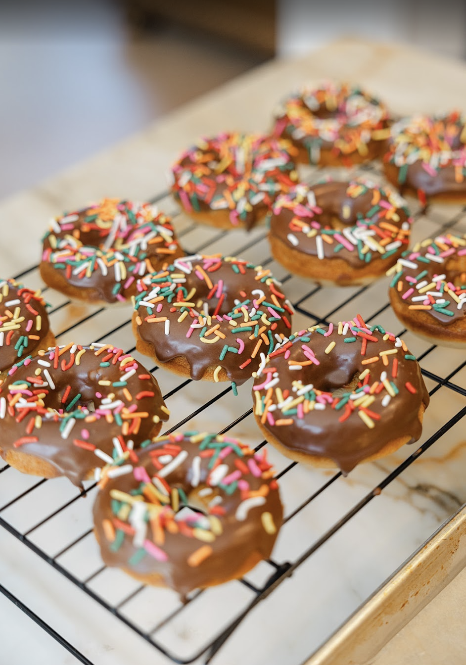Chocolate donuts with colorful sprinkles on a wire cooling rack.
