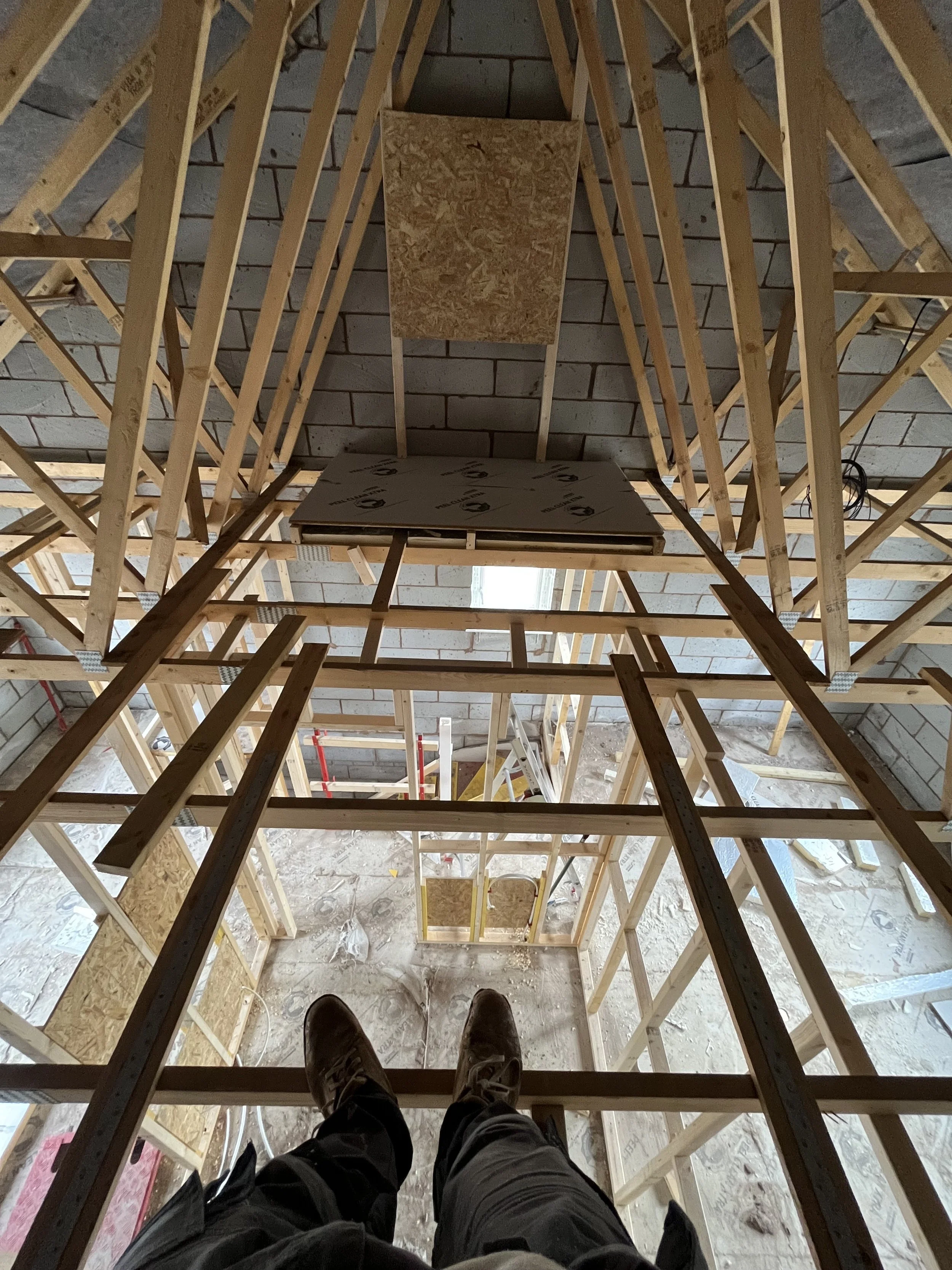 Inside view of a construction site showing a partly built wooden staircase with a view down through the framing of the building to the basement floor and exterior wall.