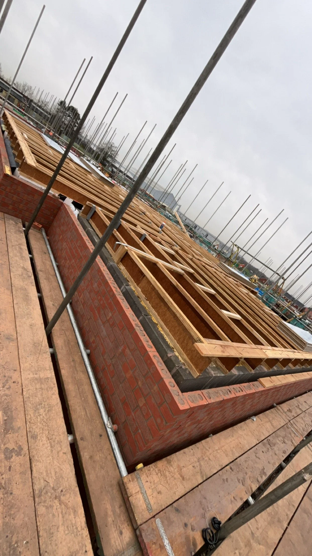 Under construction wooden framework and brick walls at a building site near a waterfront on a cloudy day.