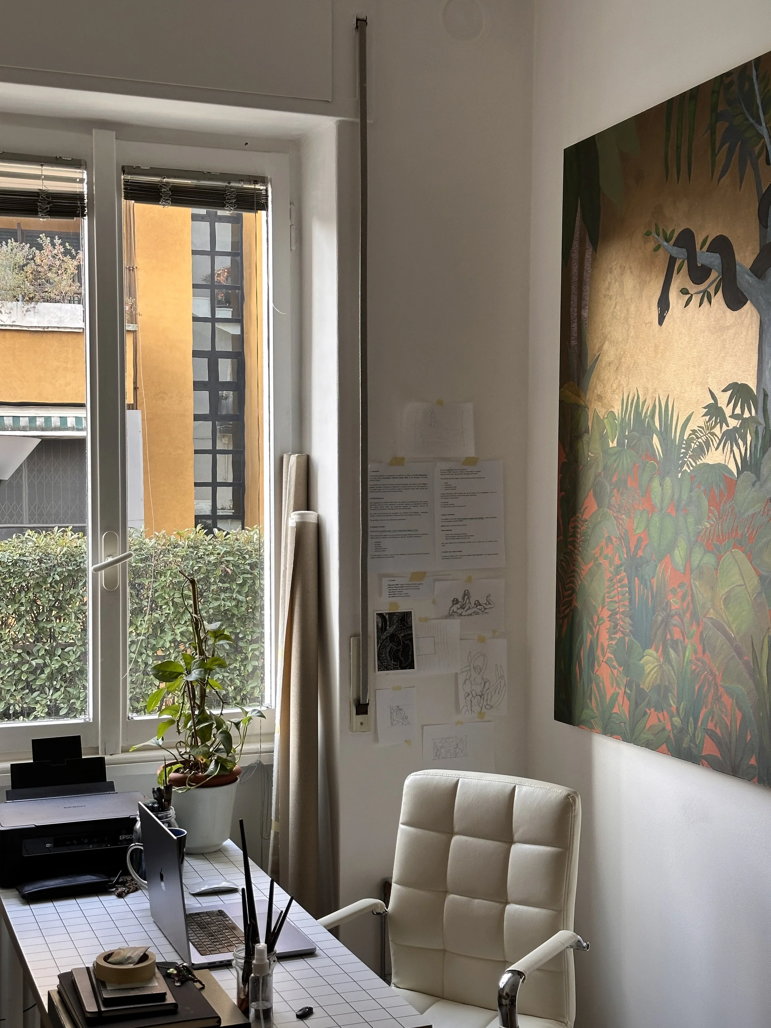 An office with a window, a white desk, a beige office chair, a large colorful jungle-themed painting, and various papers and office supplies on the desk.