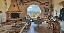 Living room with a round window showing a scenic view outside, fireplace, armchair, coffee table, and decorative shelves.