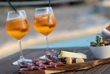 Two glasses of iced tea, a charcuterie board with sliced meats, cheese, and grapes, and a small bowl of nuts on a table.