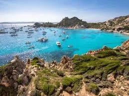 A scenic view of a bay with turquoise water, surrounded by rocky cliffs and boats anchored in the water.