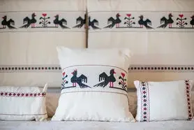 Decorative pillows on a bed with a tapestry featuring silhouette figures of people and camel riders at the headboard, in a room with neutral tones.